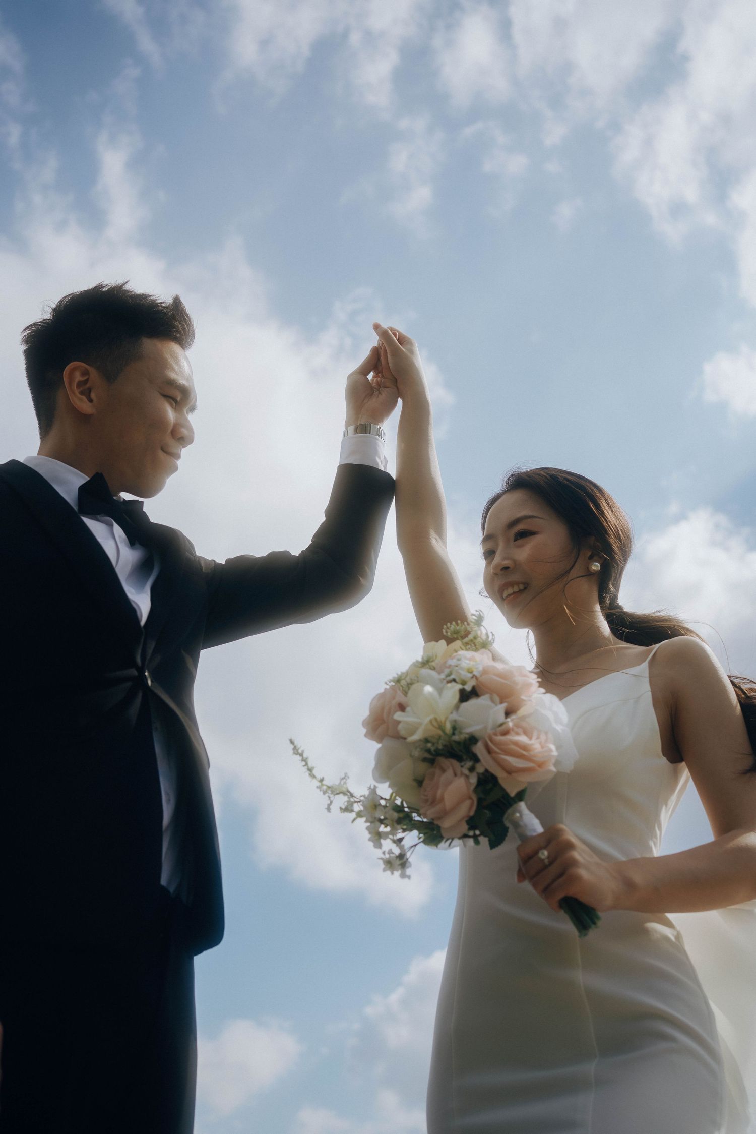 A bride and groom dance together joyfully against a cloudy sky backdrop during their wedding celebration.