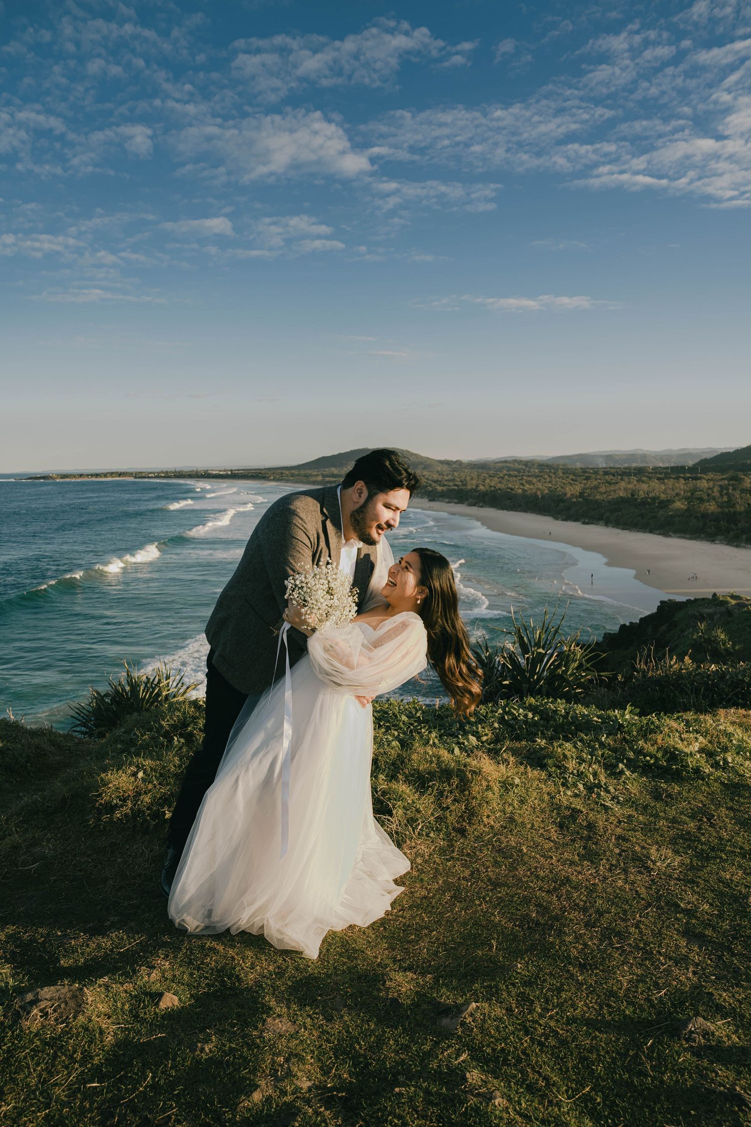 Couple shares romantic moments on coastal cliffs overlooking a scenic beach landscape at sunset.