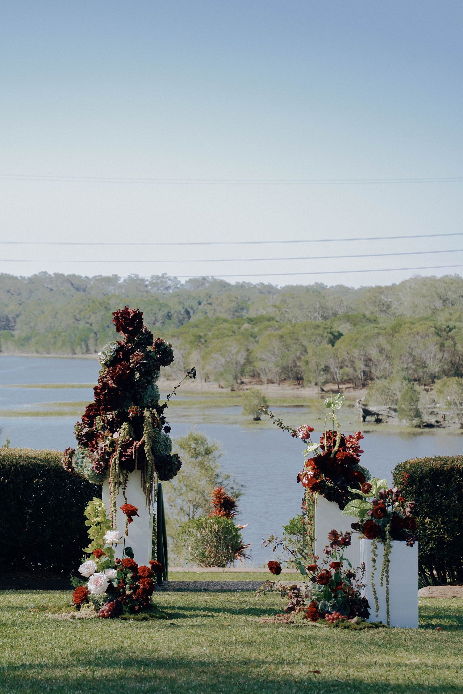 White wedding arch decorated with vibrant orange and red flowers stands elegantly against a waterfront backdrop.