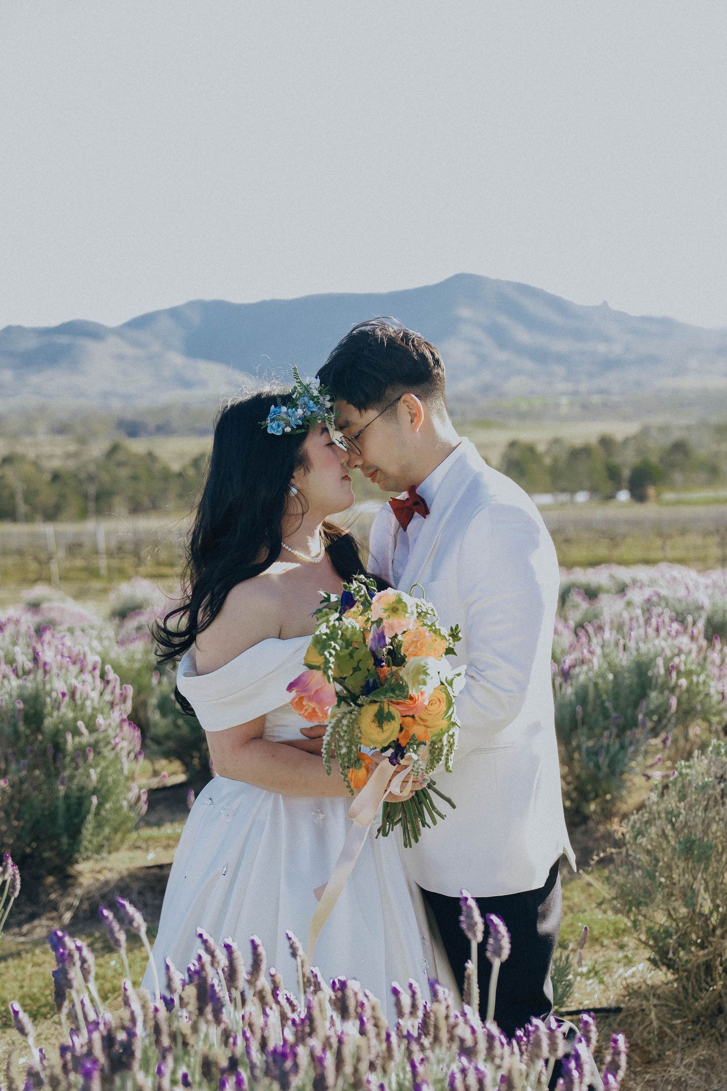 A couple shares an intimate moment among purple wildflowers with desert mountains creating a scenic backdrop.