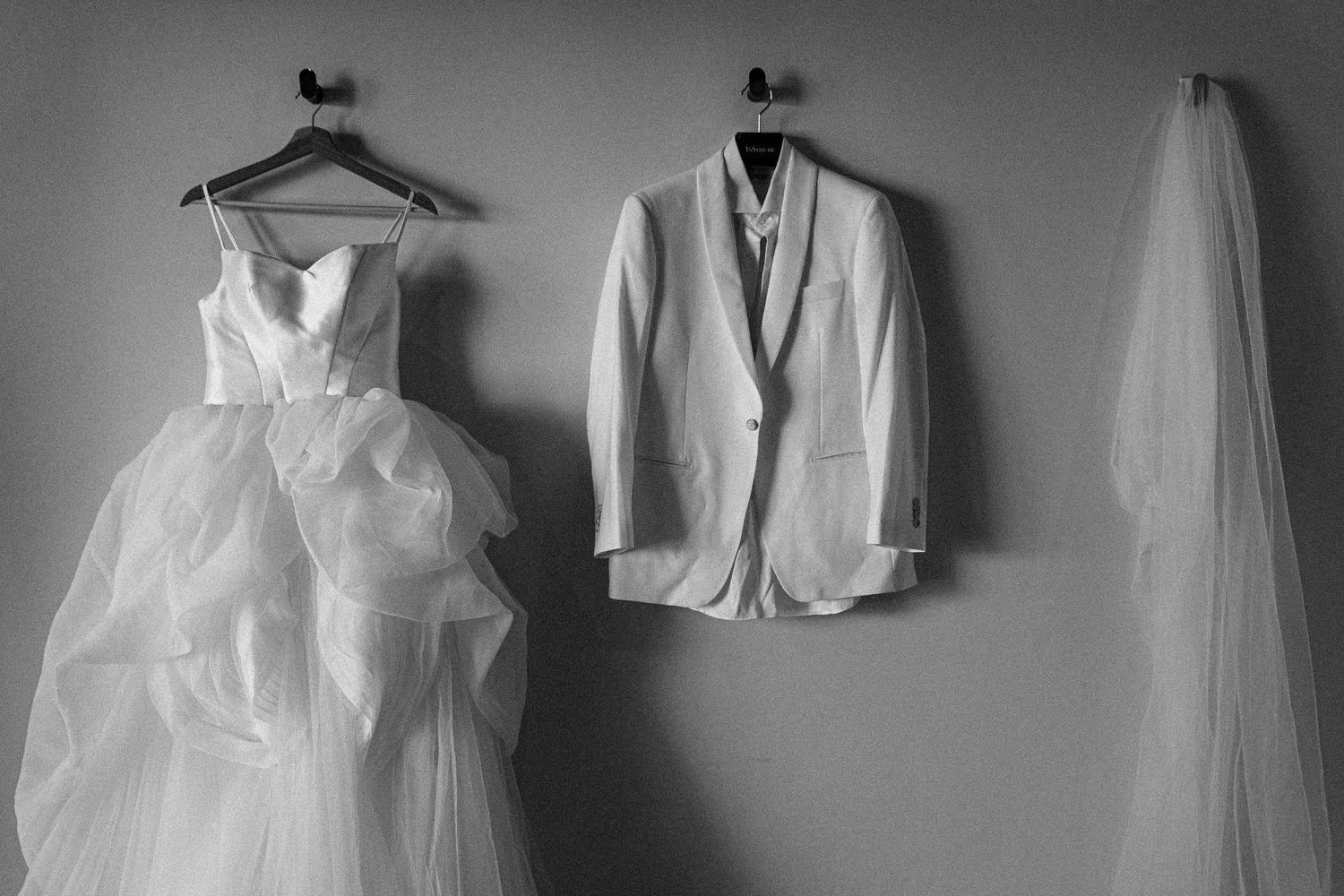 Wedding dresses and formal white attire hang on hangers against a grey wall in a boutique display.