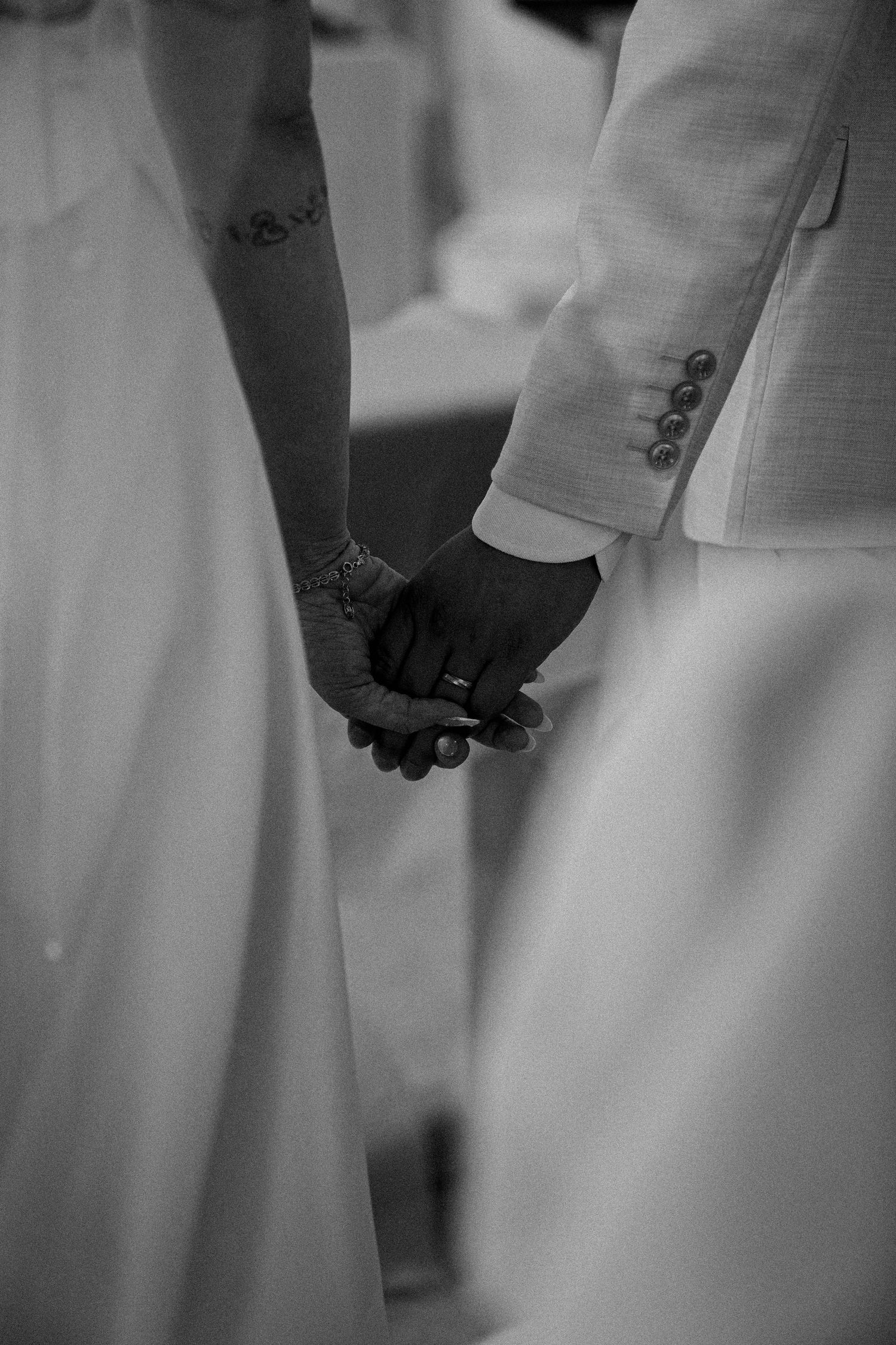 Black and white close-up of hands holding during a wedding ceremony, showing formal attire and emotional connection.