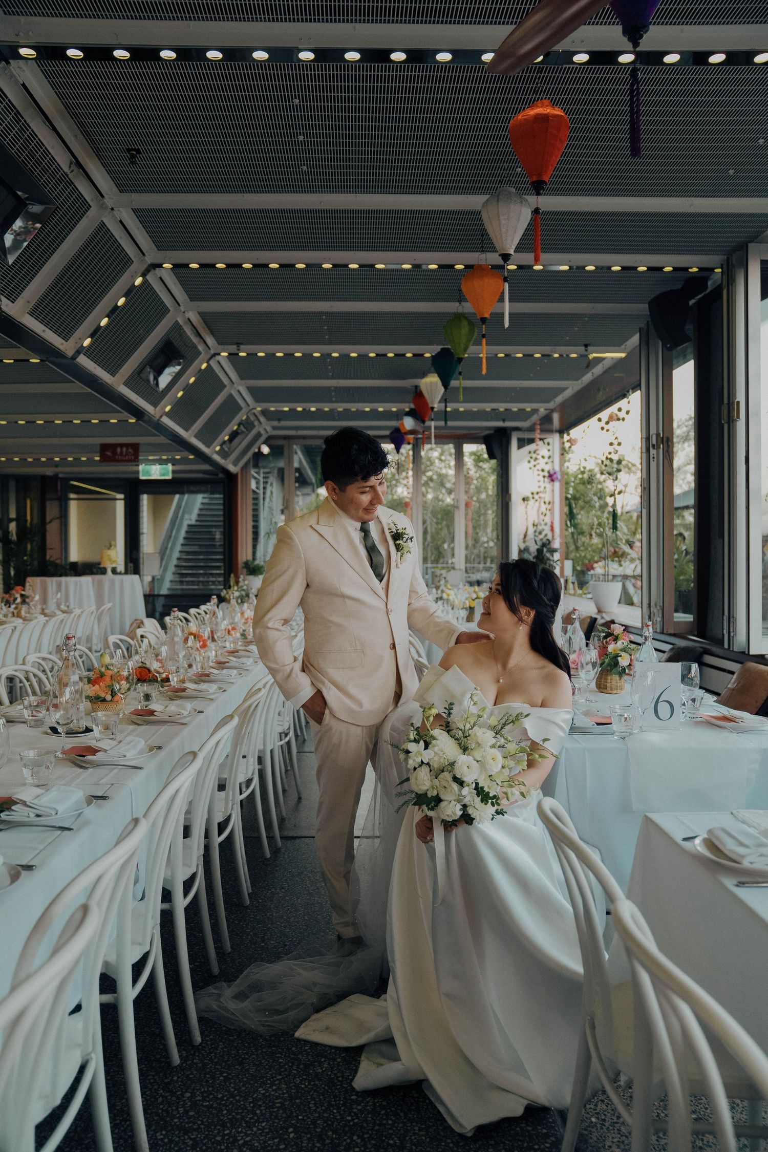 Wedding reception setup with elegant table decor and colorful paper lanterns hanging from a covered outdoor venue.