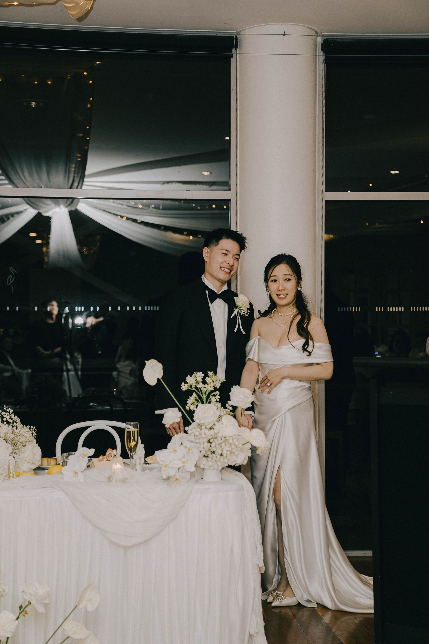 Elegant wedding reception setup with white floral centerpieces and a beautifully decorated table against a nighttime cityscape.