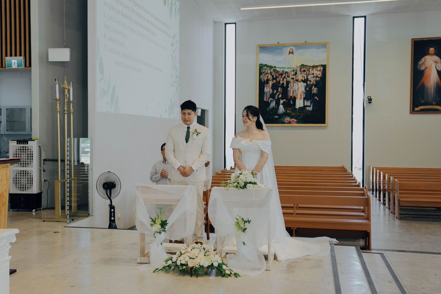 A panoramic view of a hospital waiting room with wooden benches, white walls, and floral arrangements.