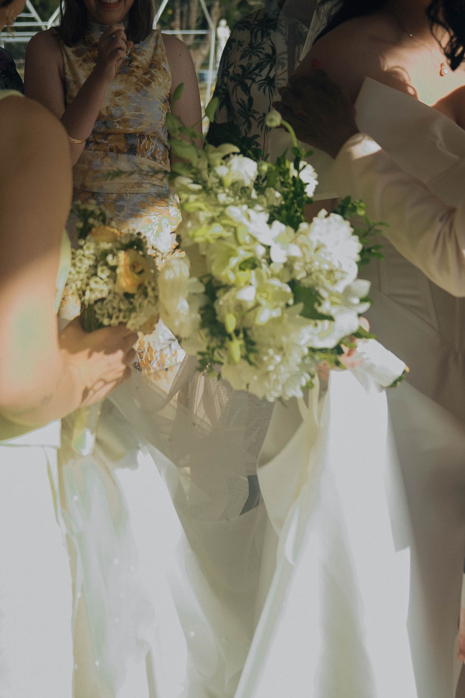 A delicate white and green wedding bouquet held against flowing white fabric in soft natural lighting.