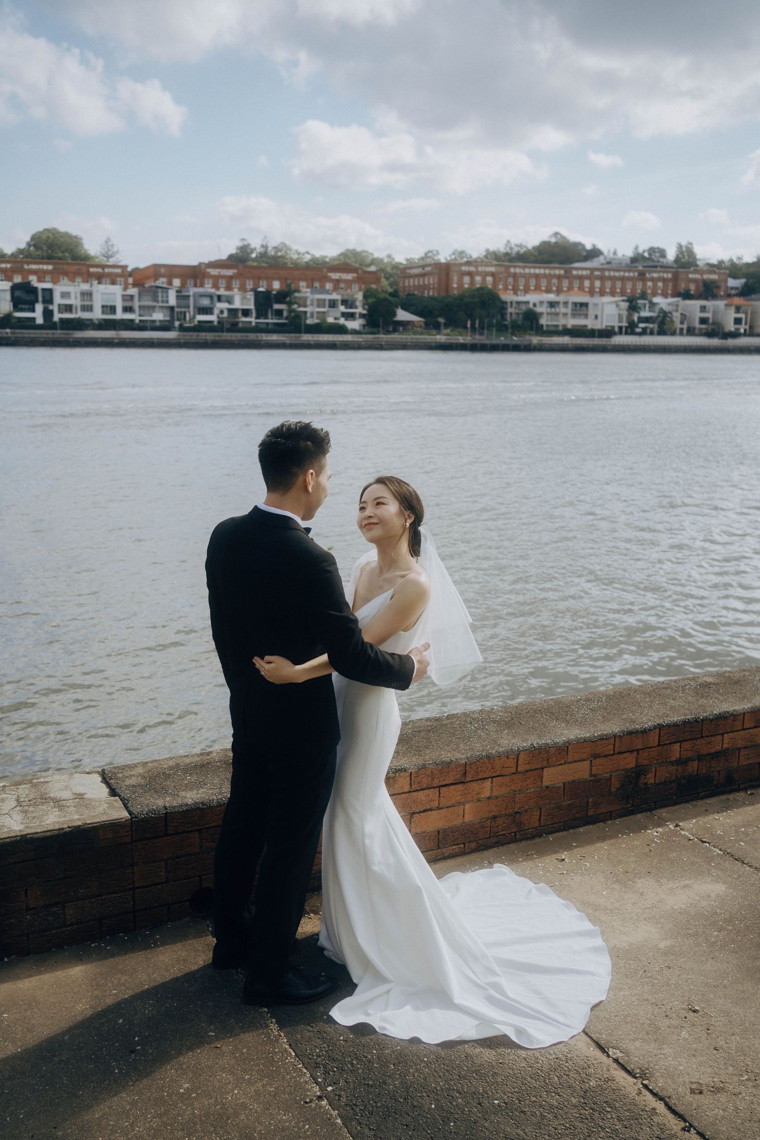 A bride and groom share an intimate moment together on a waterfront promenade with buildings in the background.
