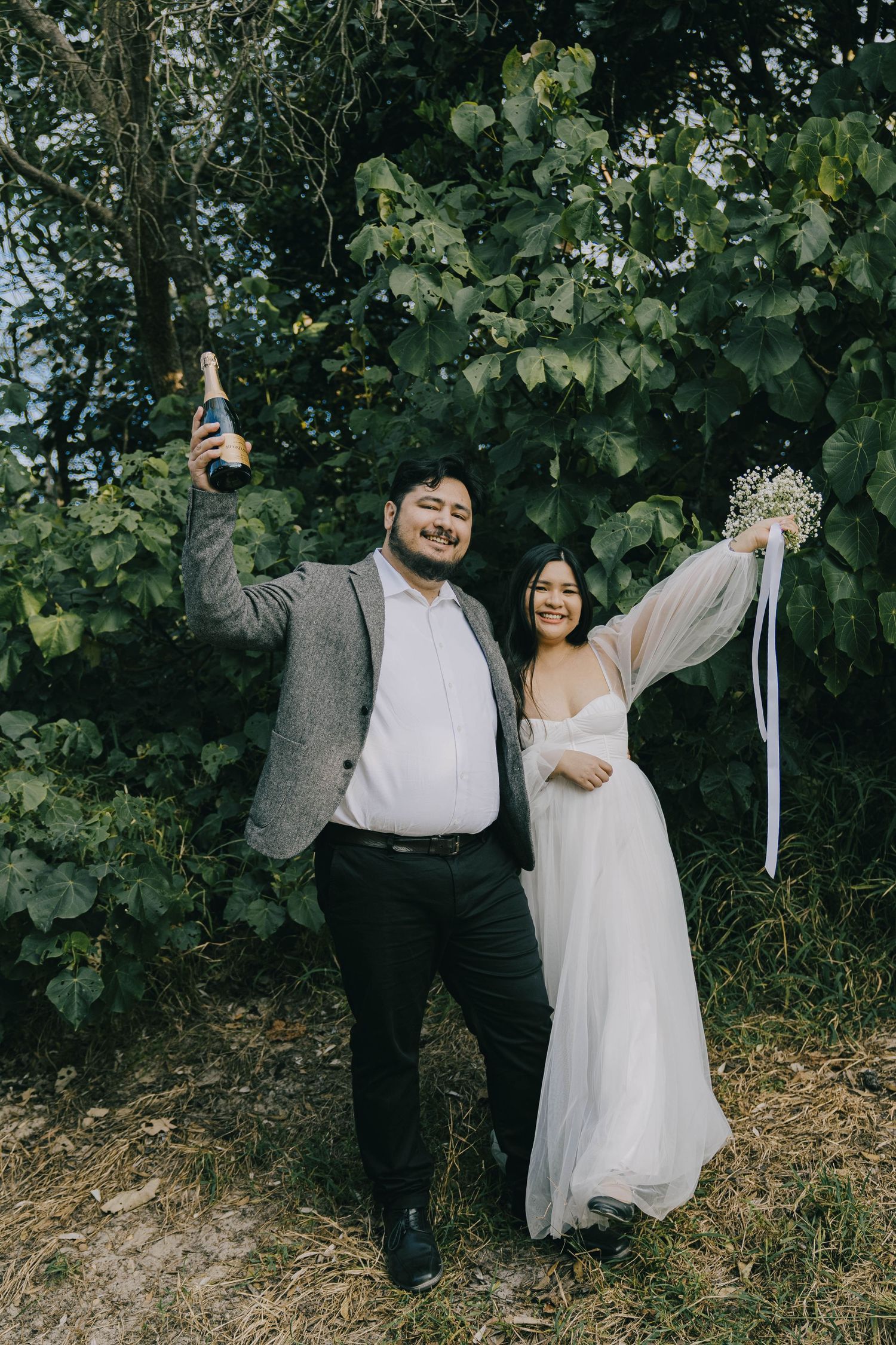 A couple in wedding attire playfully poses in front of green foliage in a series of candid outdoor shots.