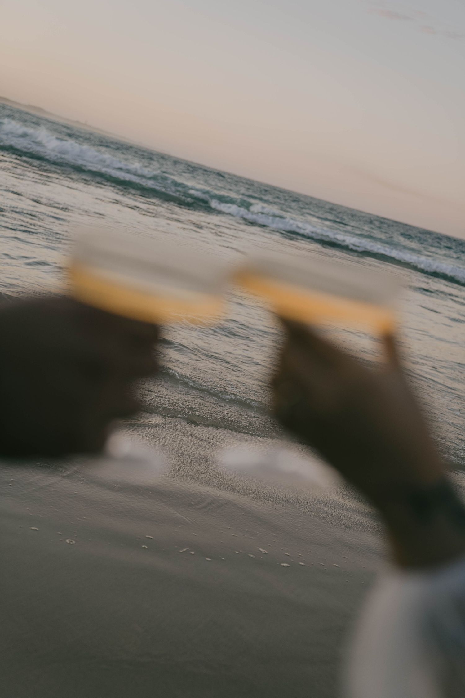 Blurred motion sequence of ocean waves at sunset with silhouetted figures on the beach creating a dreamy atmosphere.