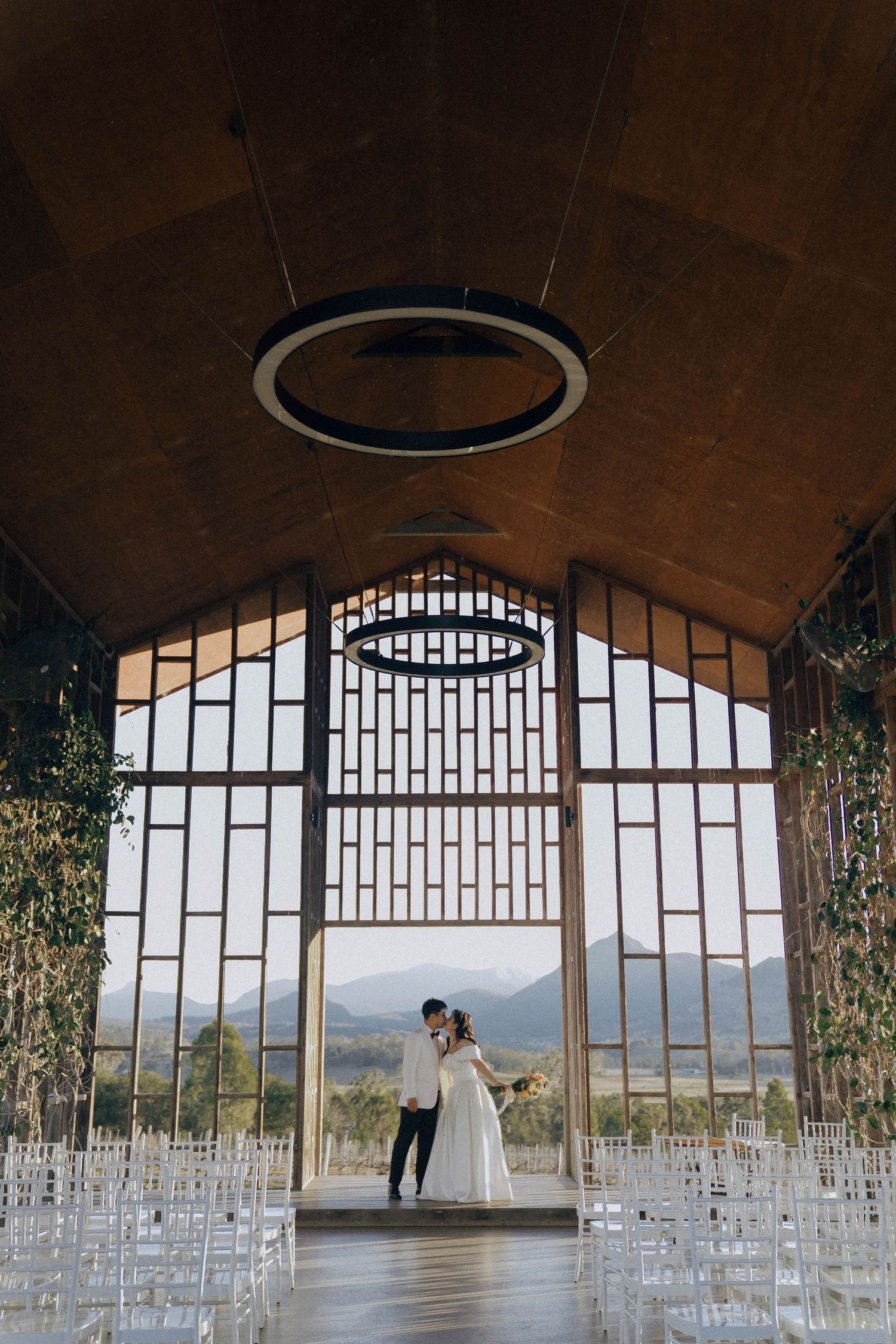 Panoramic view of an elegant indoor wedding venue with rows of white chairs and large windows overlooking mountain scenery.