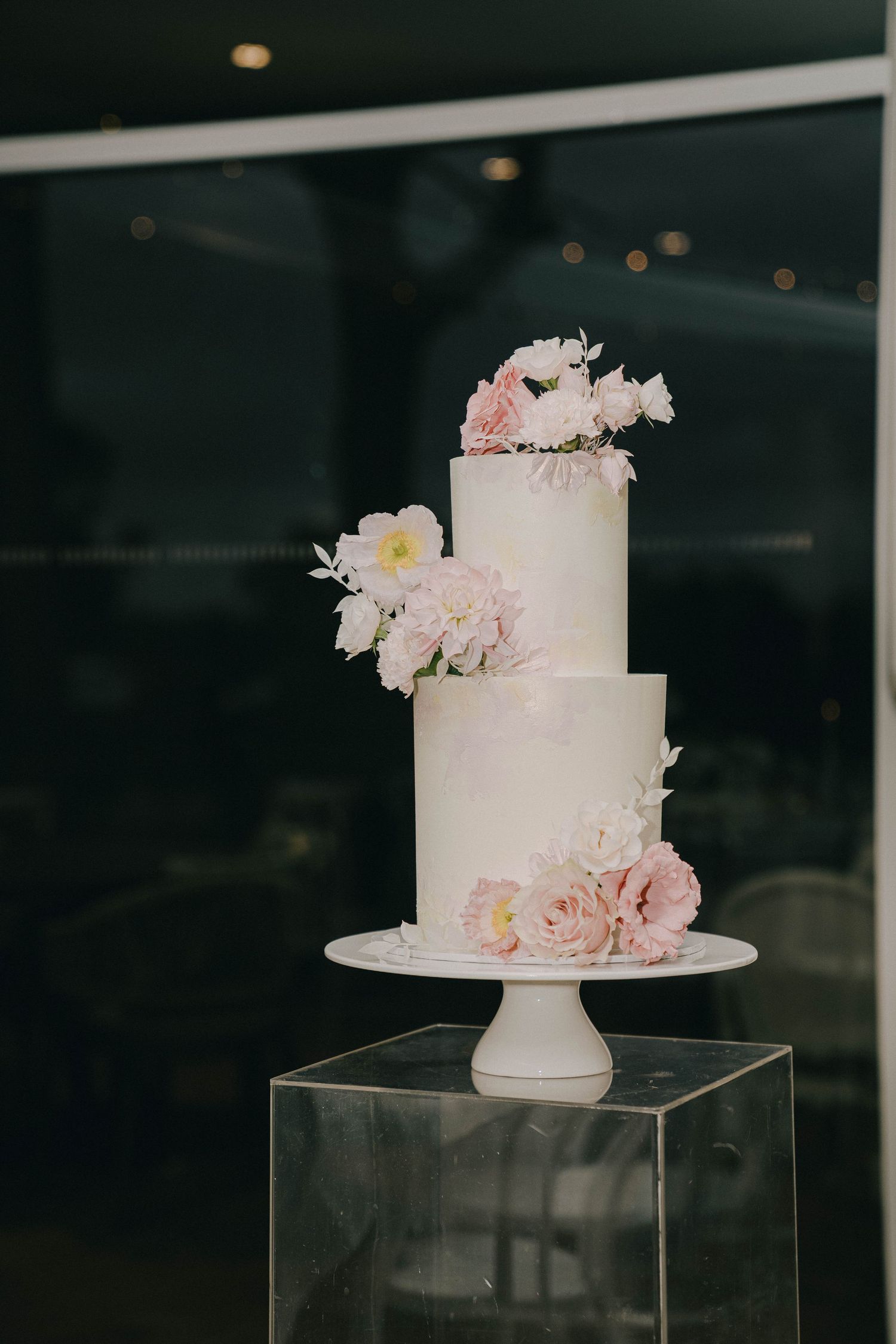 Elegant white wedding cake decorated with delicate pink and white flowers displayed on clear acrylic stands.