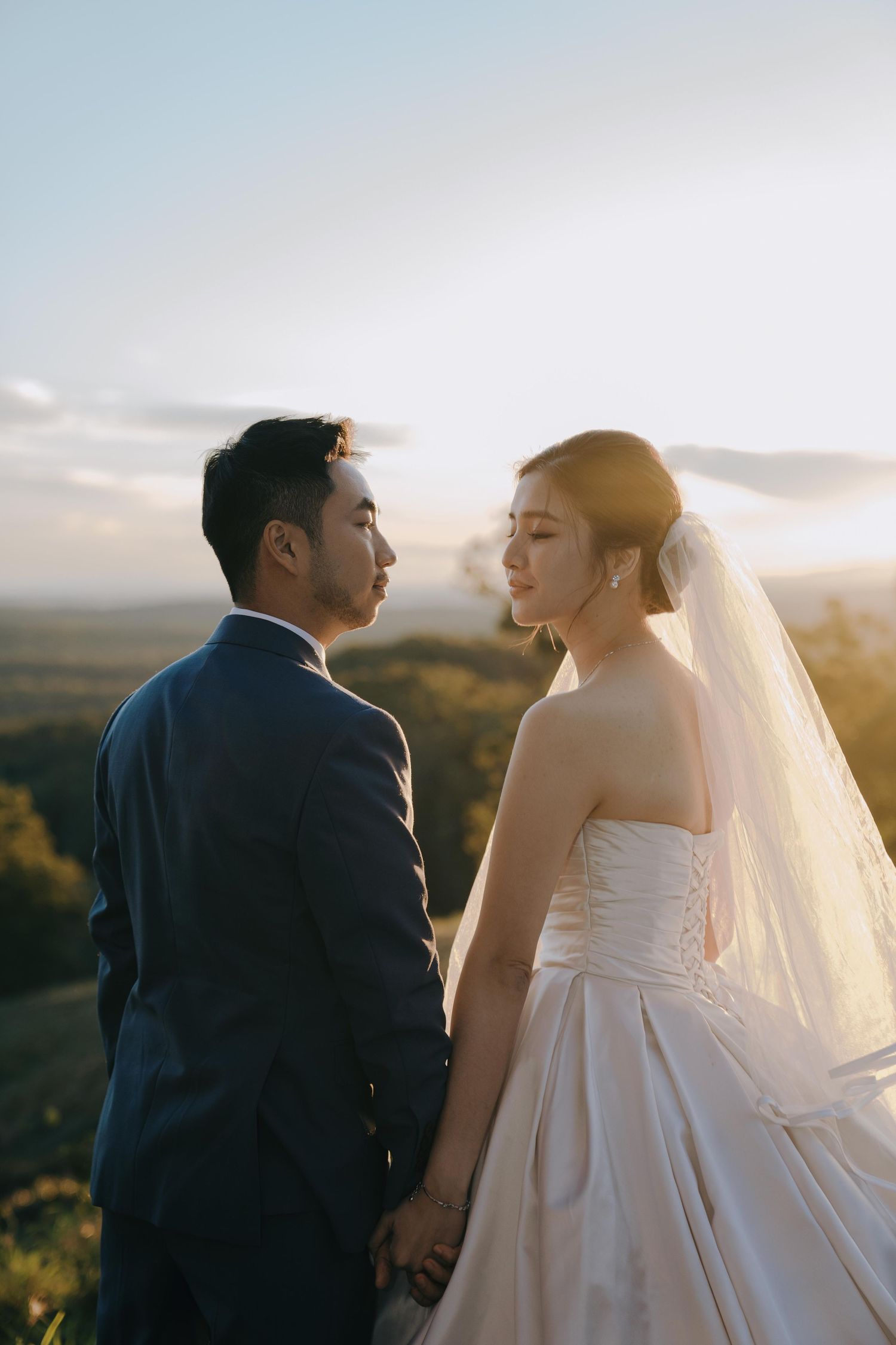 Wedding couple shares intimate moments at sunset against a scenic mountain backdrop with flowing veil and white gown.