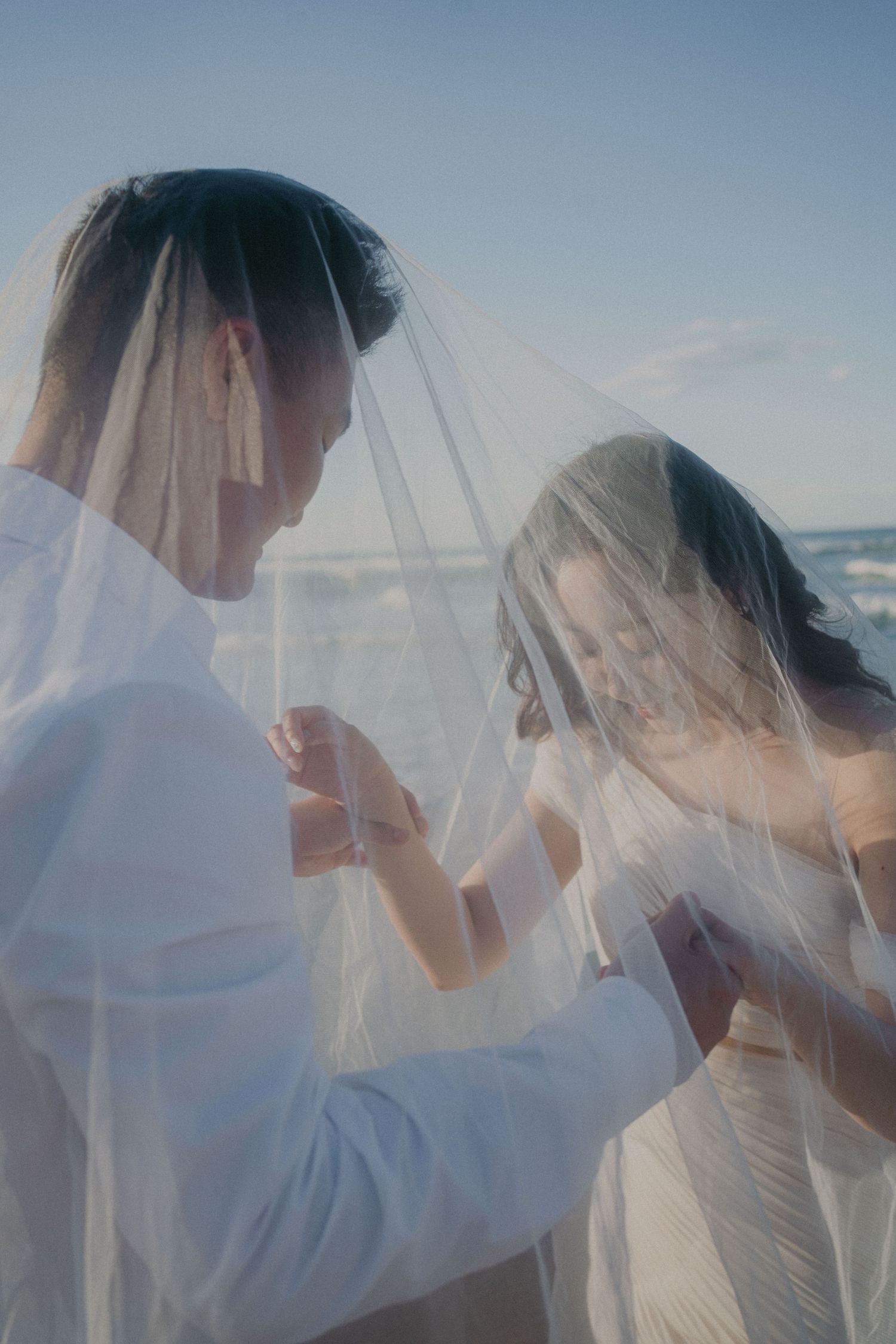 Three soft, romantic beach wedding photos showing intimate moments between a couple beneath a delicate white veil.
