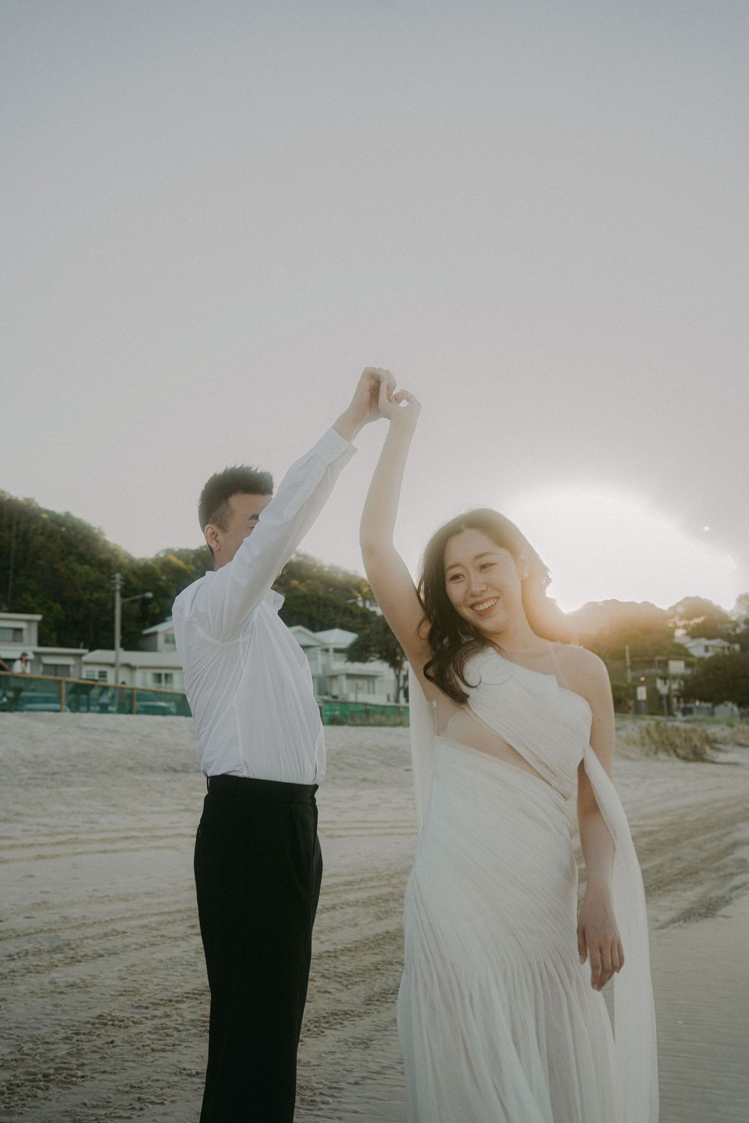 A couple dancing together on a beach at sunset, with the bride in a flowing white dress twirling gracefully.