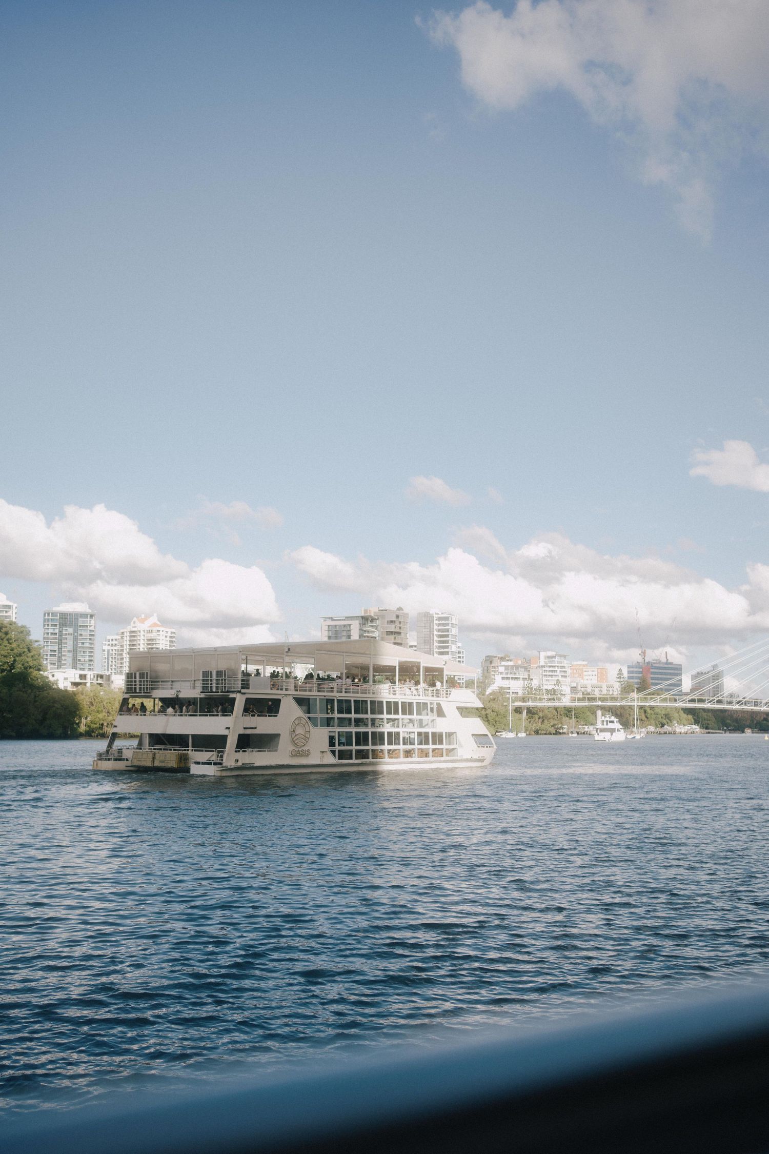 Panoramic sequence showing a white modern houseboat anchored in calm blue waters near city buildings under puffy clouds.