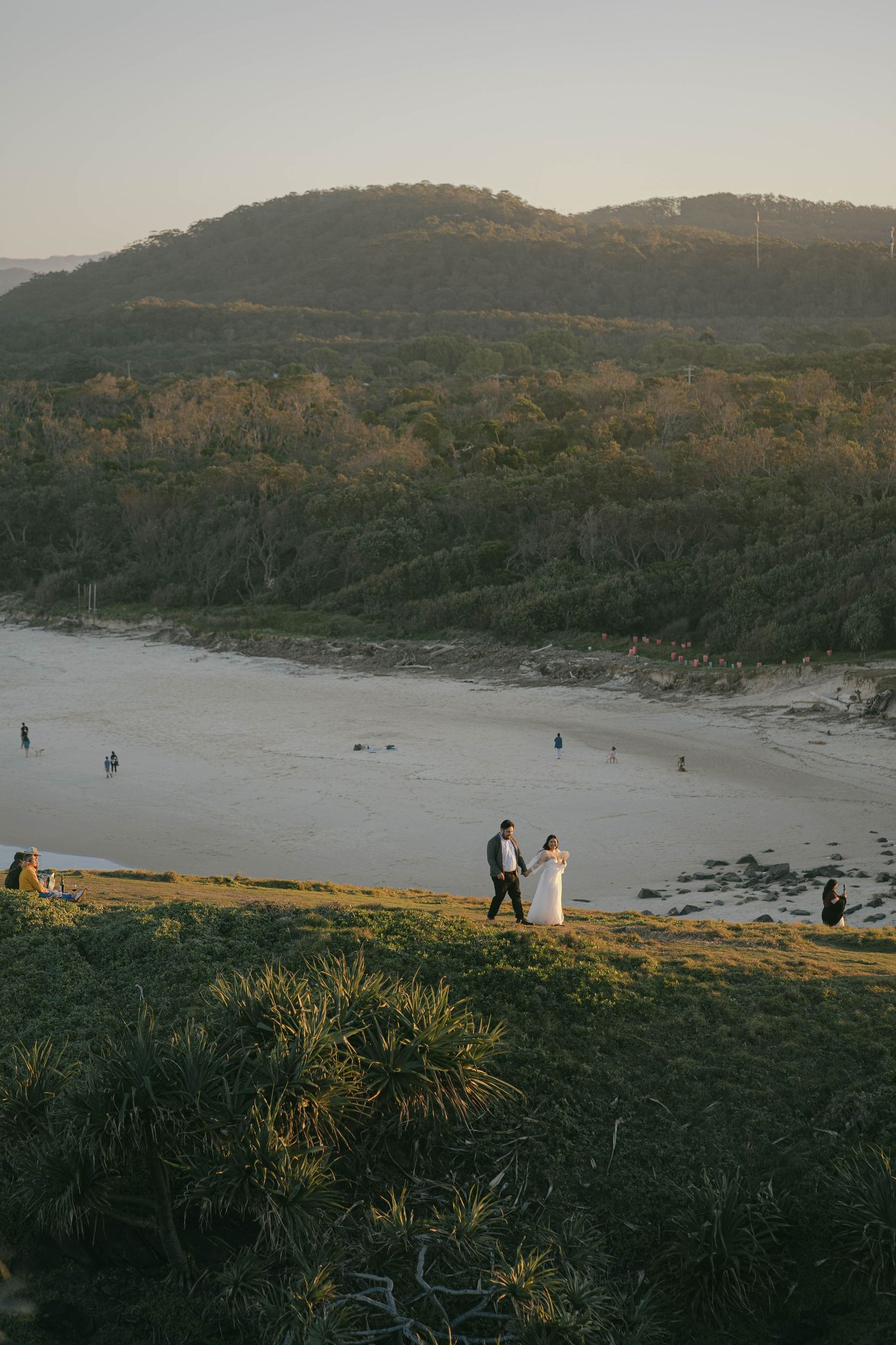 A panoramic view of a coastal landscape with rocky cliffs and beach at sunset showing distant figures on the shoreline.