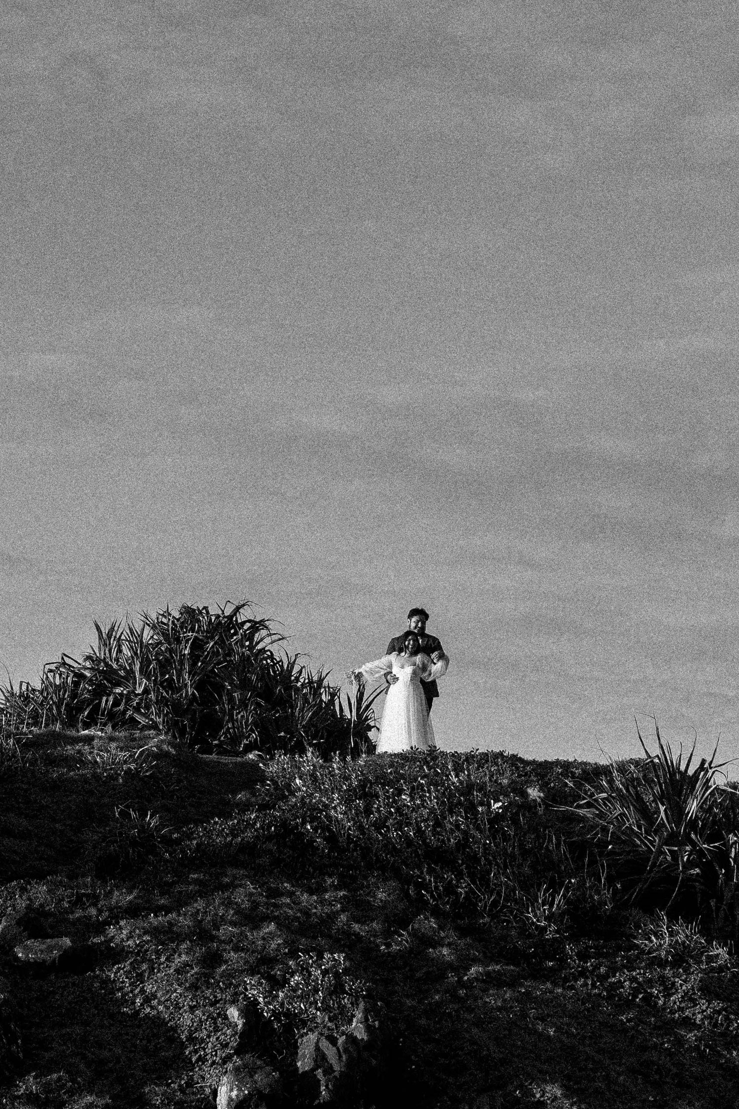A black and white panoramic view shows a silhouetted lighthouse on a hill against an overcast sky.