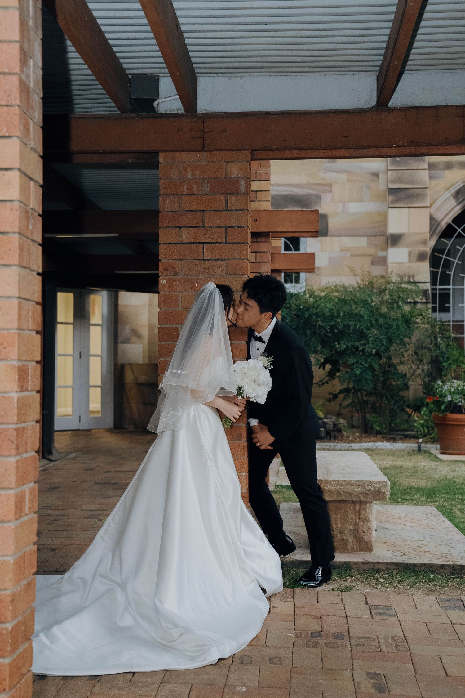A wedding couple shares intimate moments in a brick-columned courtyard during their photo session.
