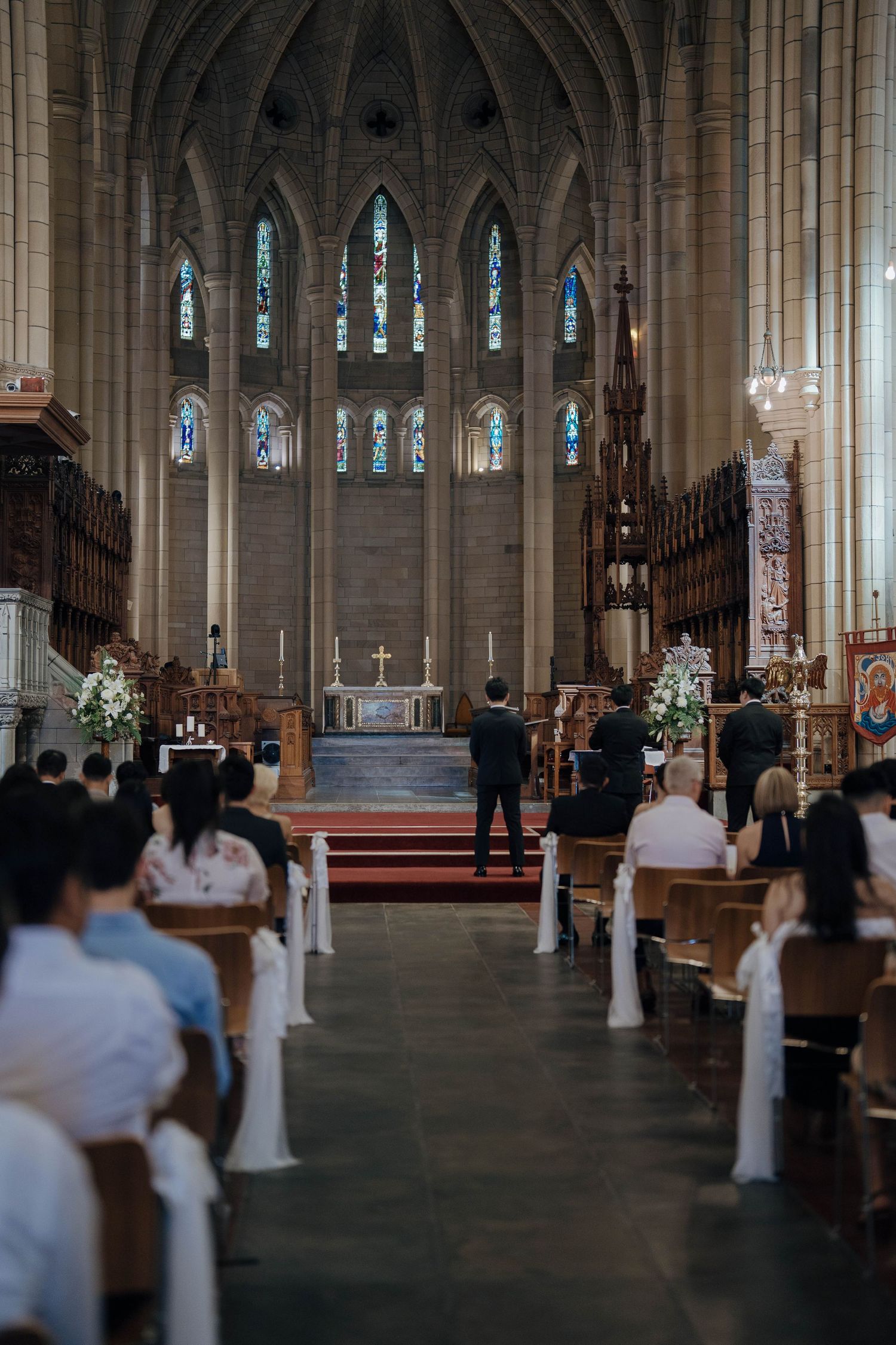 Interior view of a Gothic church during a ceremony with stained glass windows, vaulted ceilings and wooden pews.