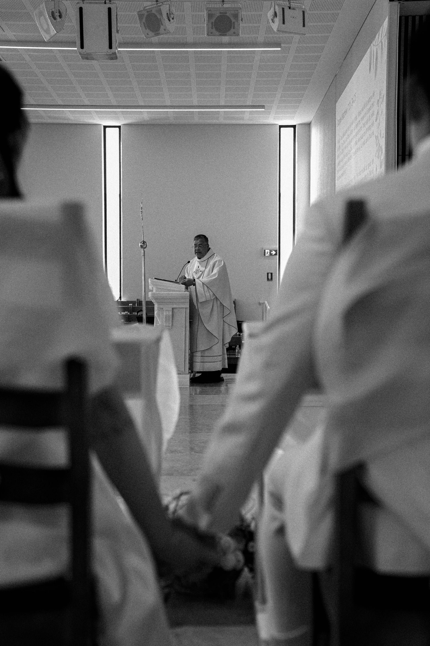 Black and white photograph of a church service showing worshippers in white clothing viewed from behind facing an altar.