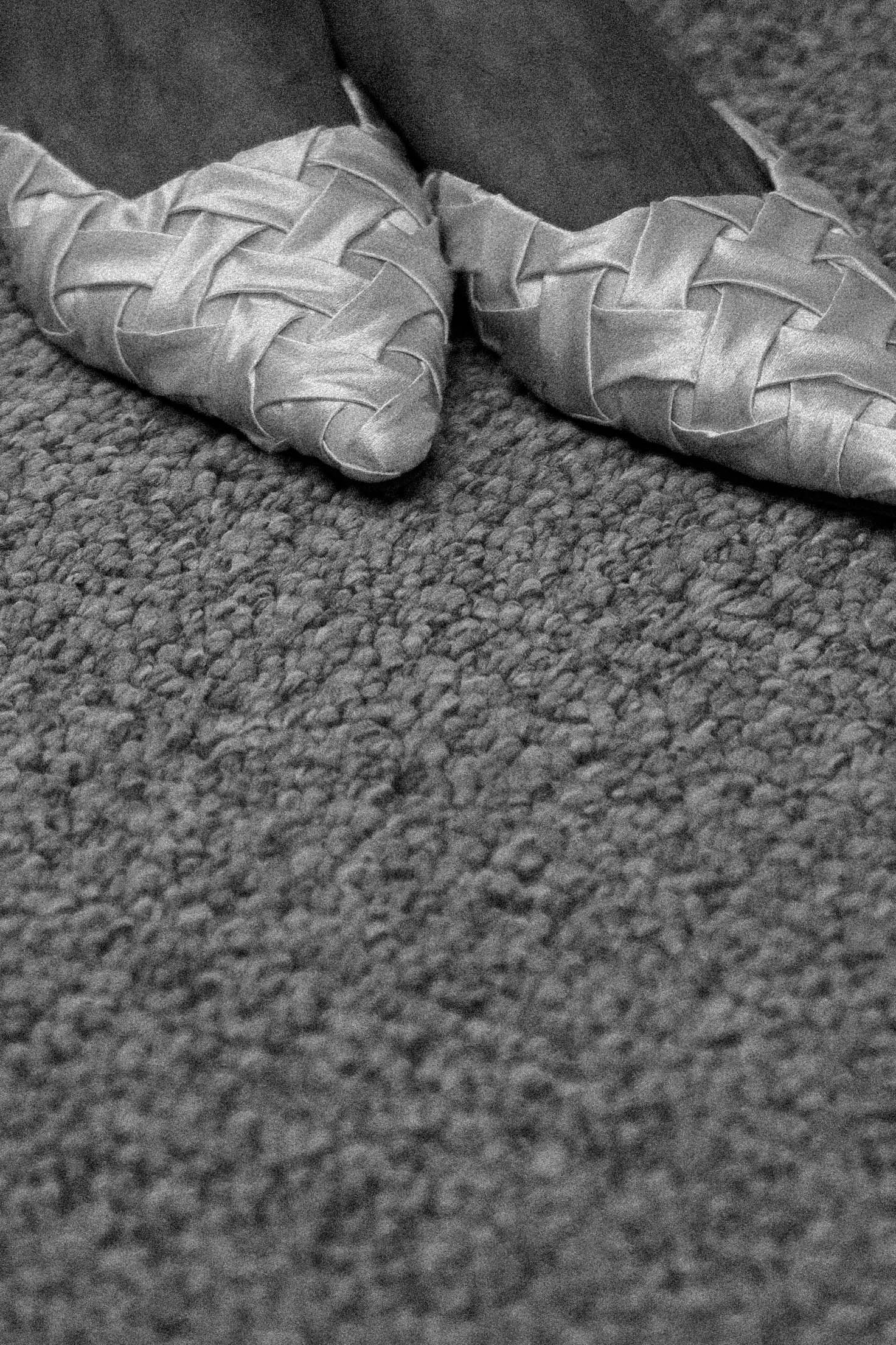 Close-up view of white leather ballet shoes resting on a textured gray carpet.