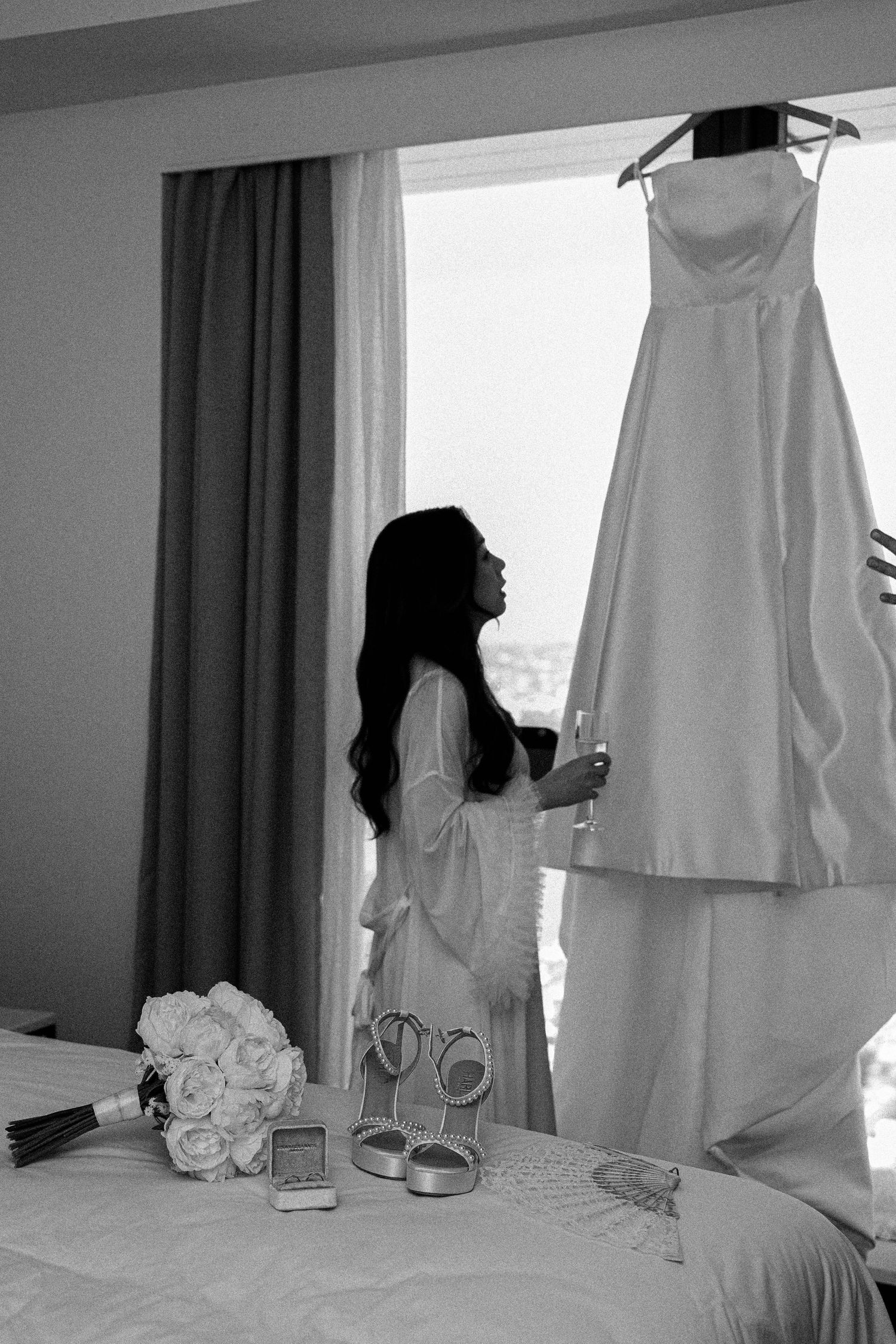 Black and white photo series showing a person hanging a white garment on a curtain rod in a bedroom.