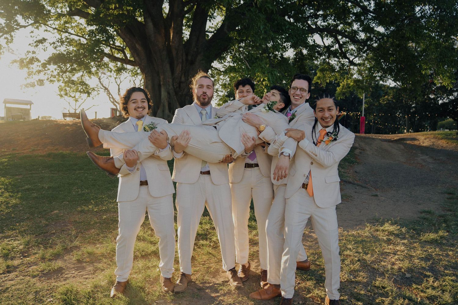 A group wearing coordinated white outfits poses together outdoors in a natural setting during golden hour.
