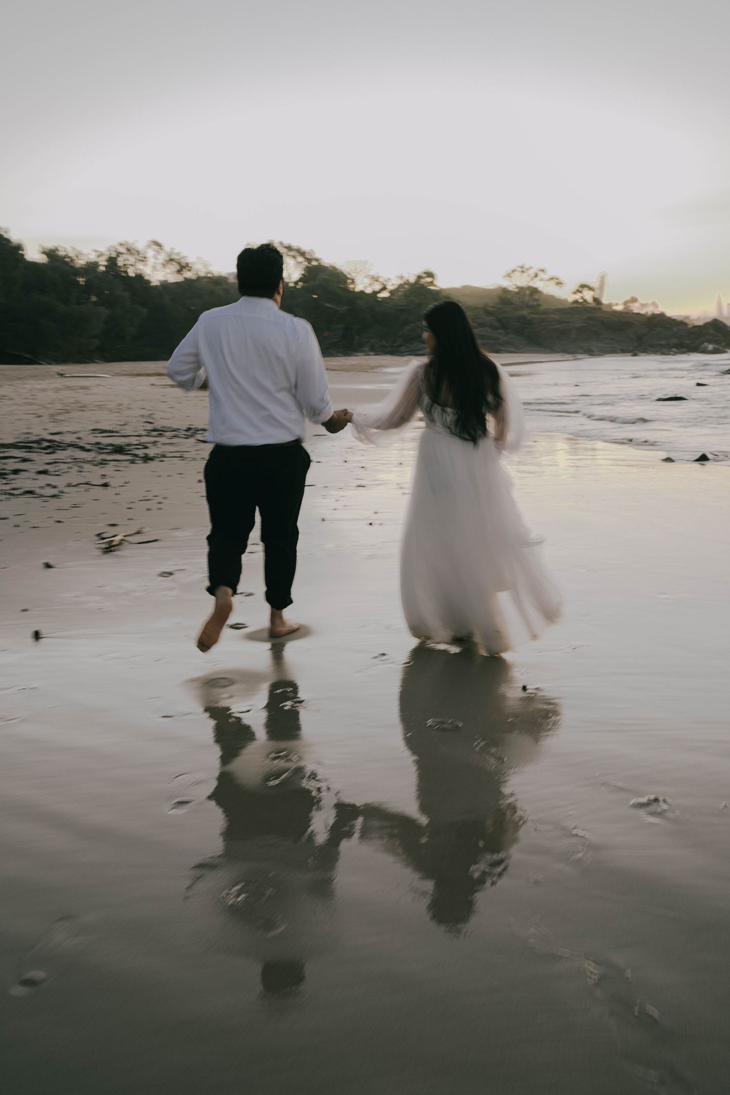 A couple runs playfully along the beach at sunset, leaving footprints in the wet sand.