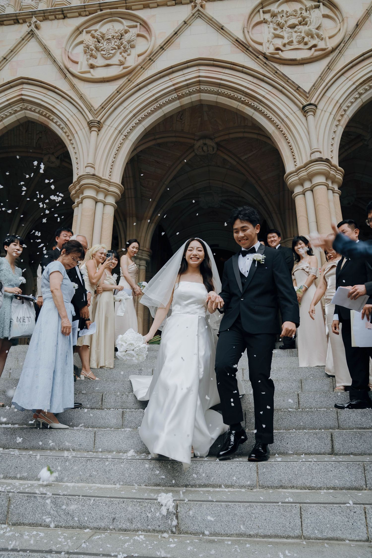 Wedding party descends stone church steps while guests throw confetti during a joyful celebration.