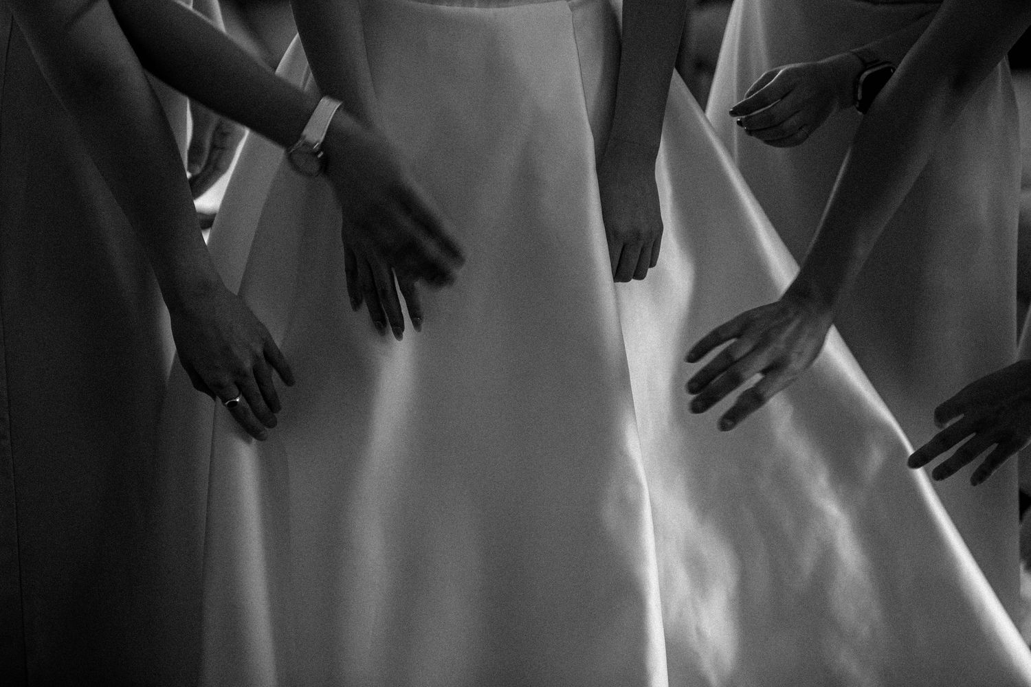Black and white image showing hands adjusting a wedding dress in dramatic lighting.