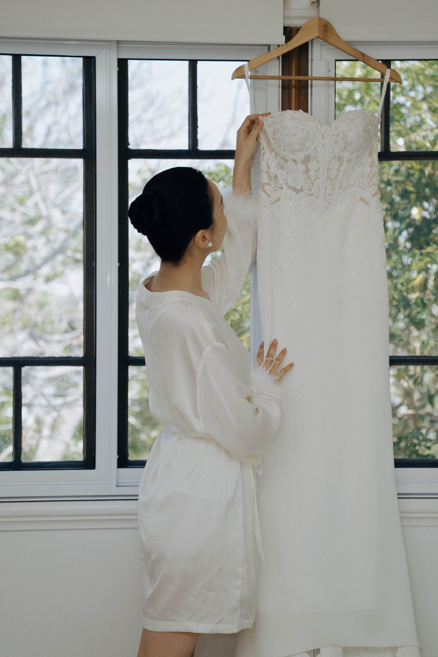 A person in a white shirt hangs delicate lace curtains on windows in a bright, sunlit room.