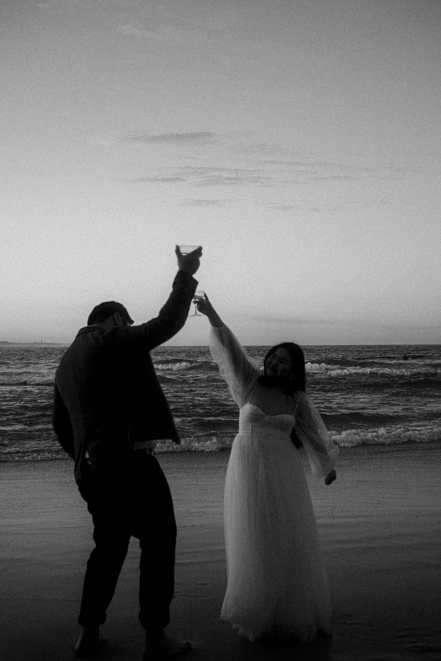 A couple dances together on a beach at sunset in a series of black and white silhouette photos.