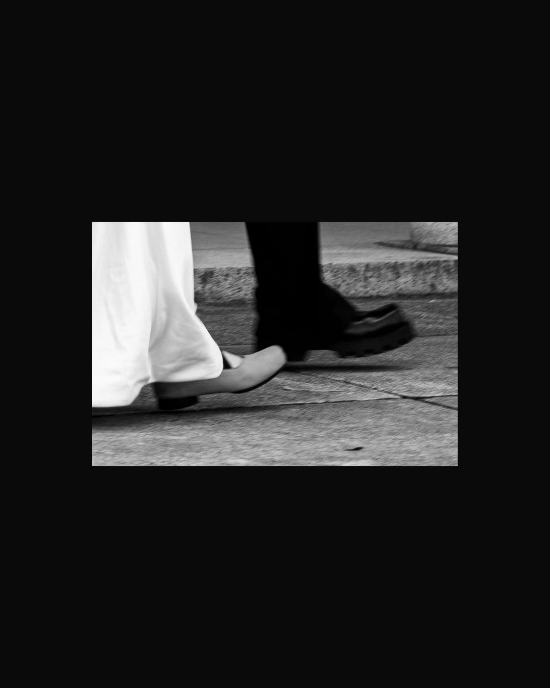 Black and white close-up photograph of two contrasting feet in shoes, one in black footwear and one in white.