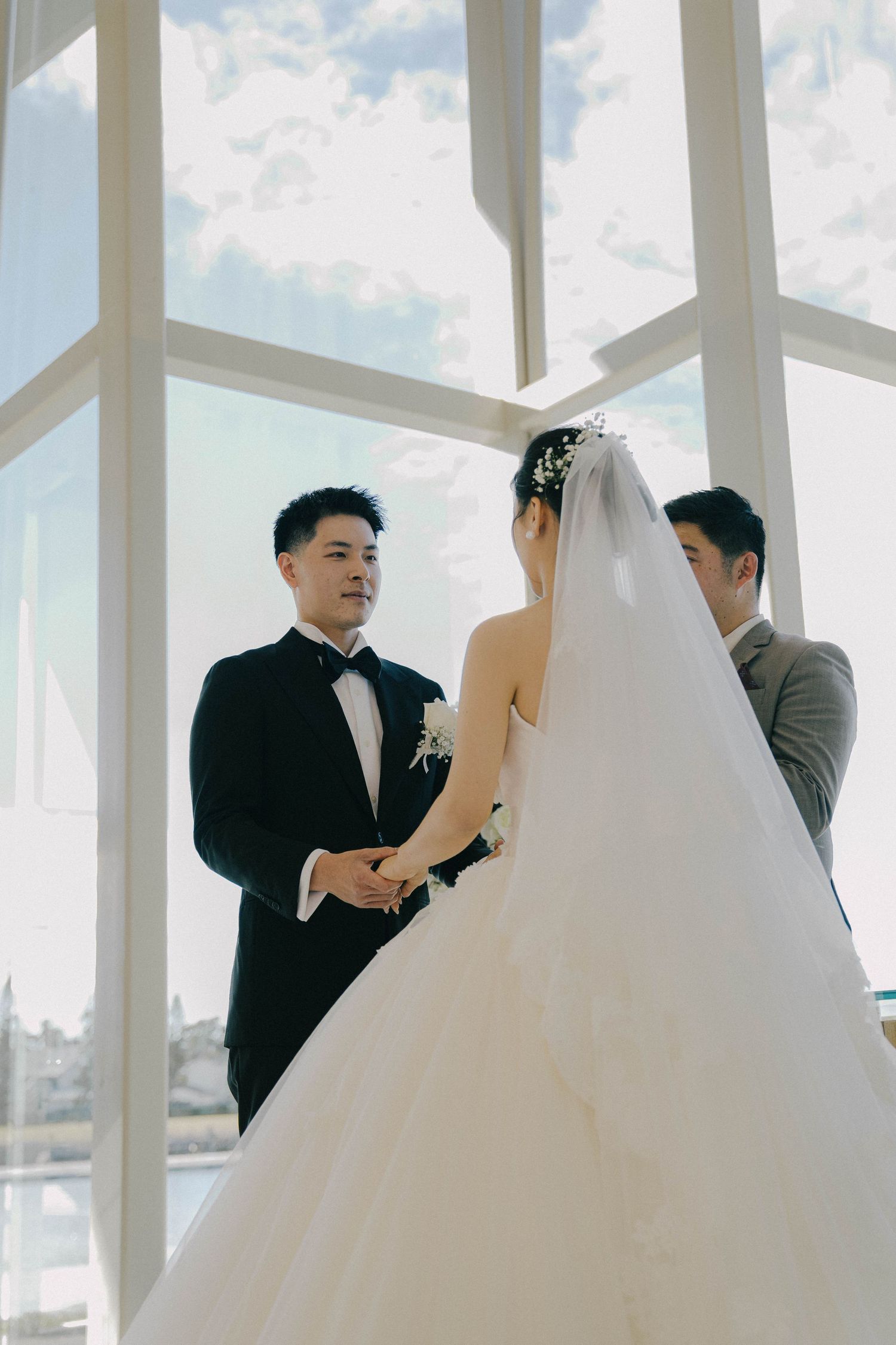 A bride and groom share a tender moment in a bright white modern space with large windows.