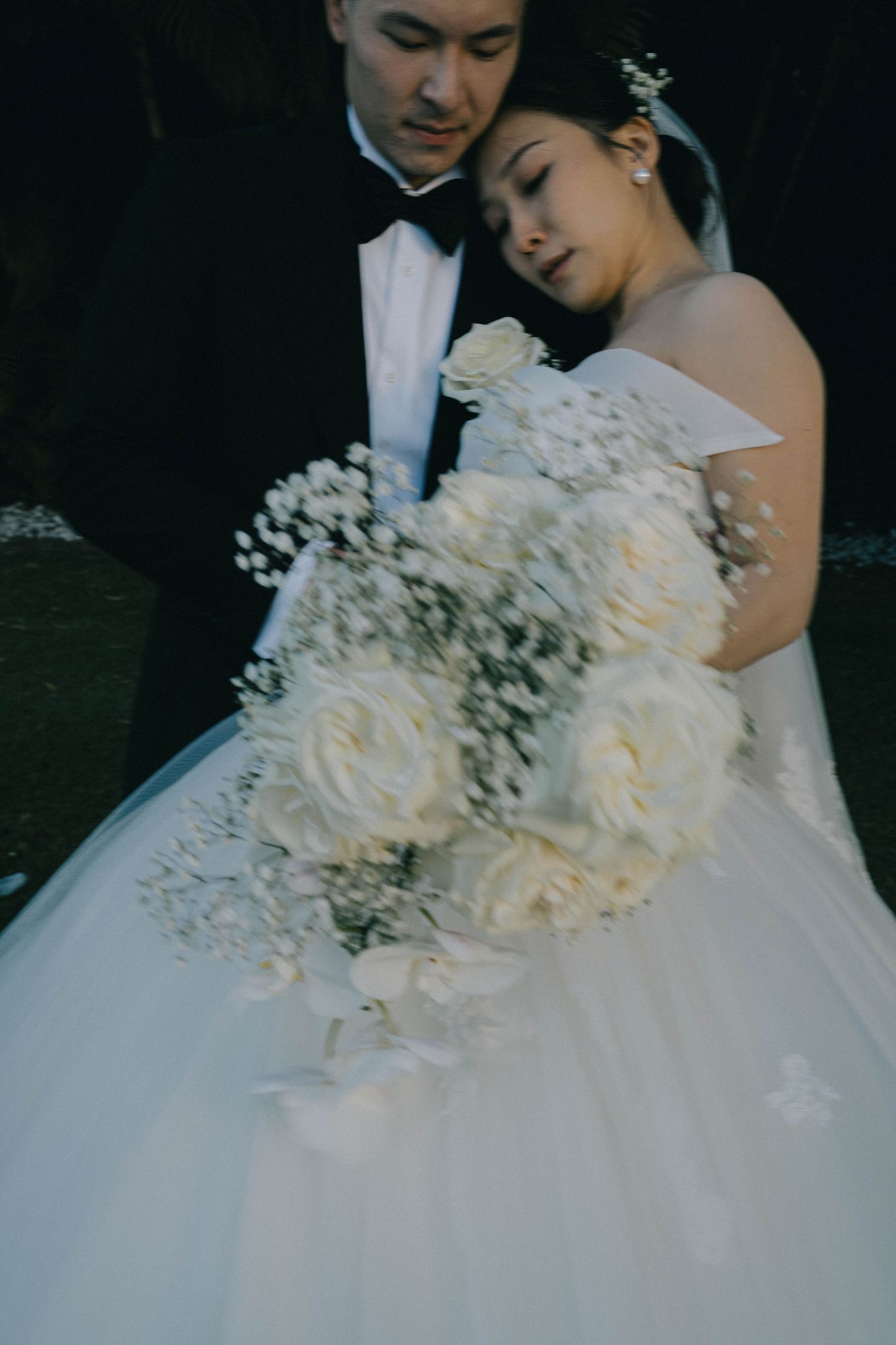 A romantic wedding couple embraces while the bride wears an elegant white gown with delicate floral details.