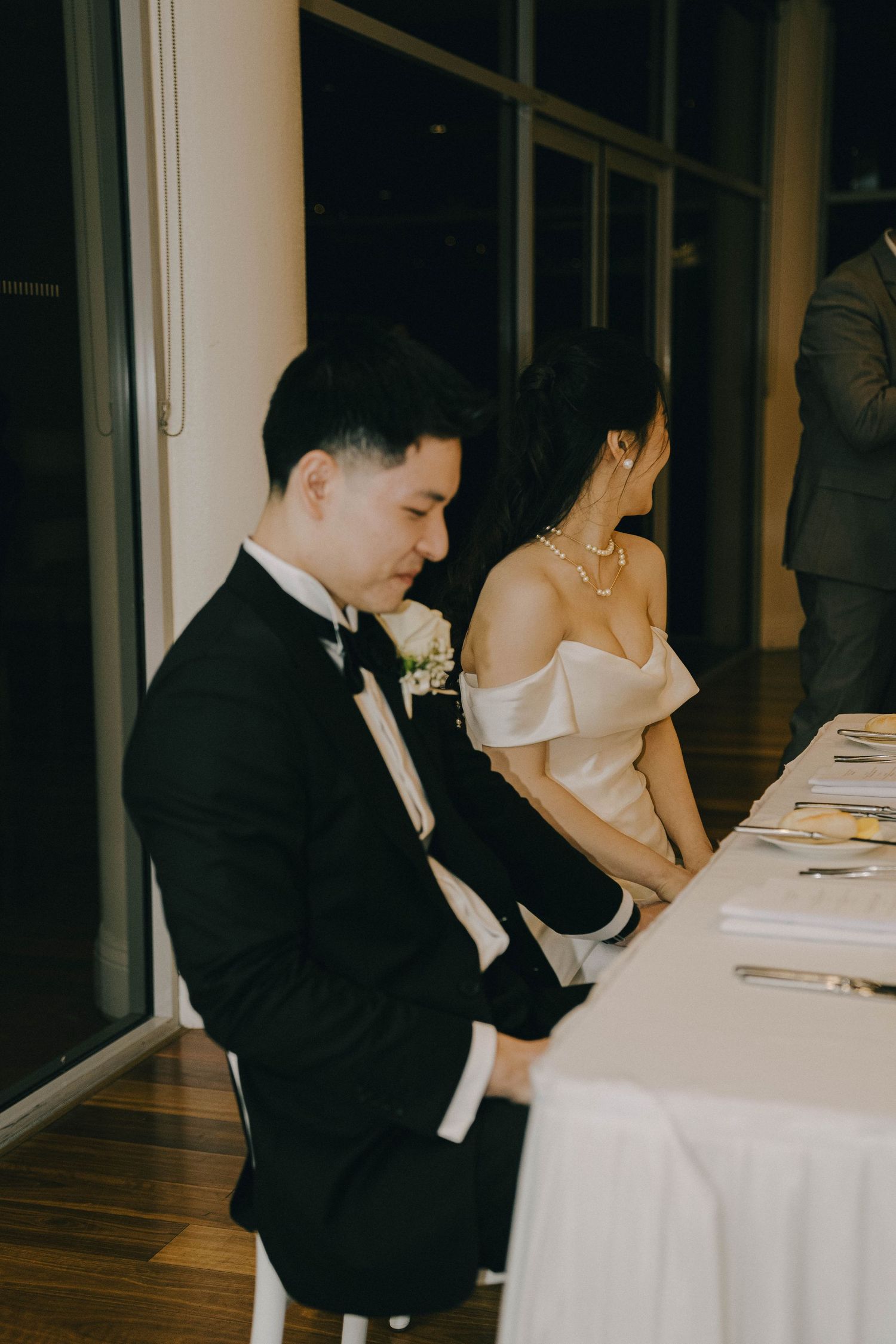 Couple in formal wedding attire sitting at a white-clothed table during a reception.
