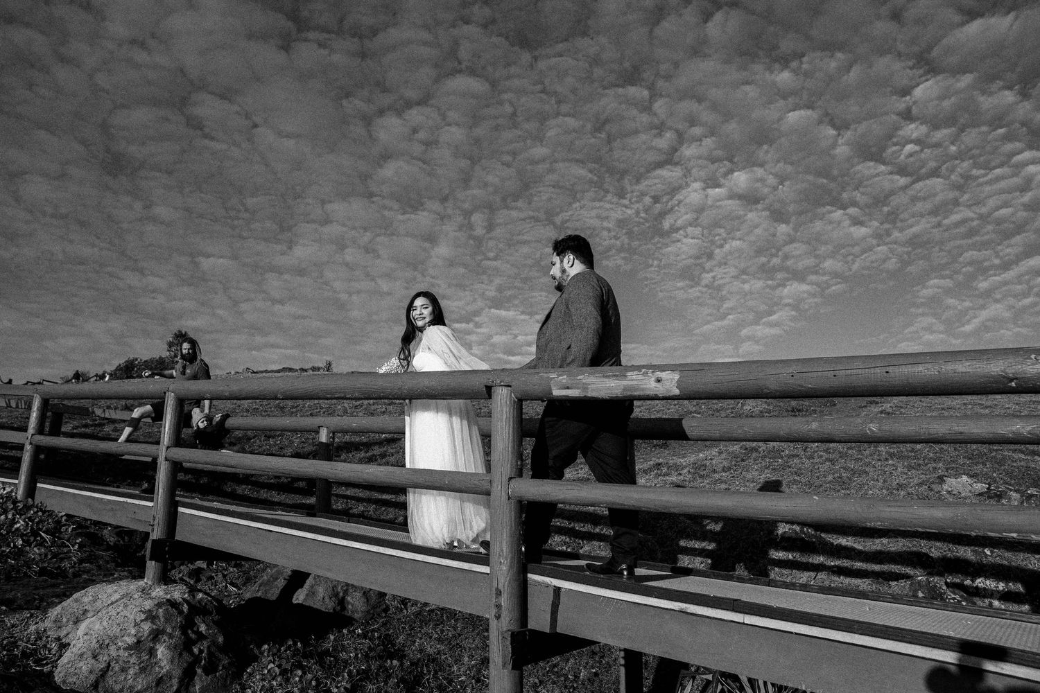 A dramatic black and white panoramic series showing a person sitting on a wooden pier over a serene lake at sunset.