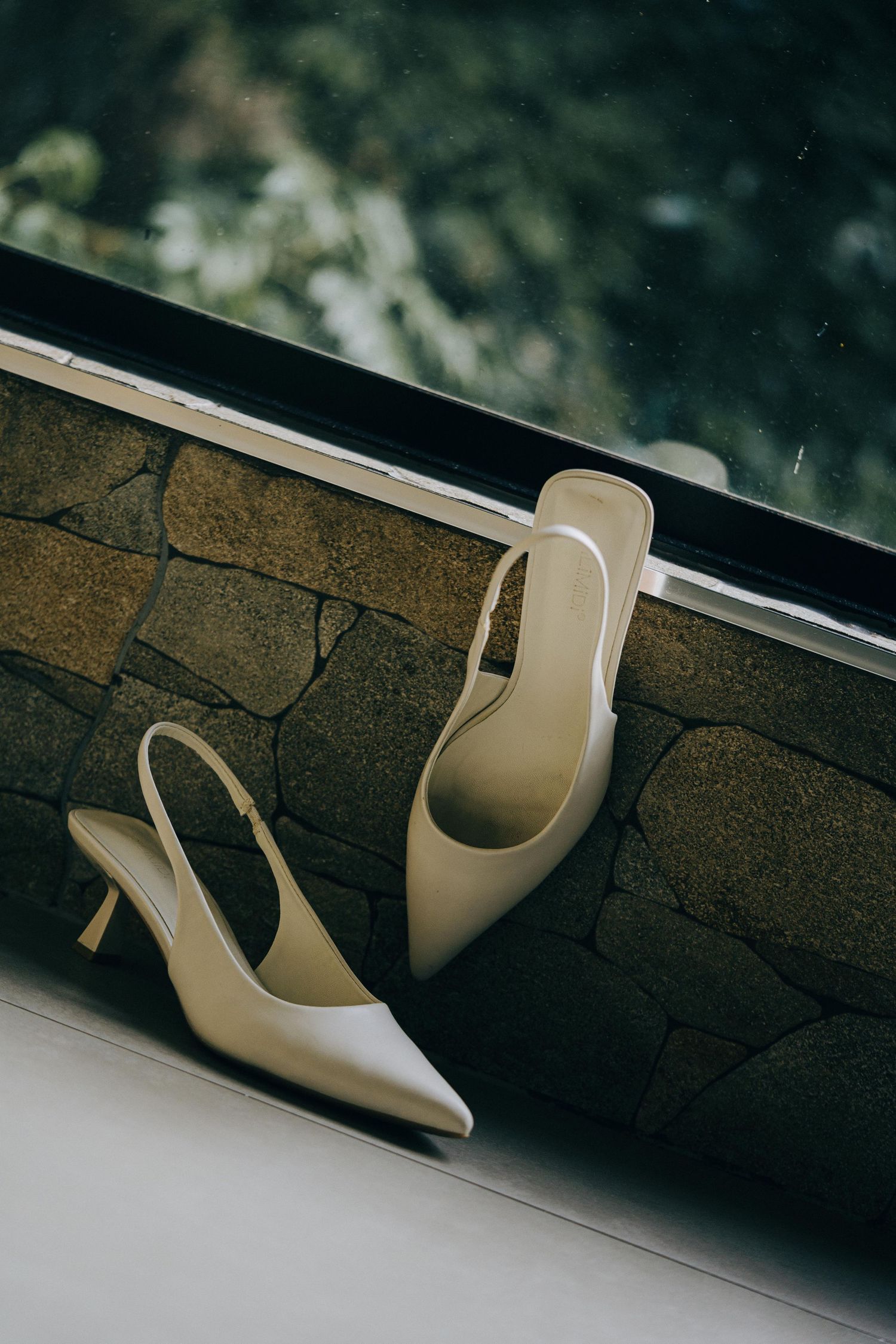 Elegant cream-colored high heel shoe displayed at different angles against a dark textured stone wall.