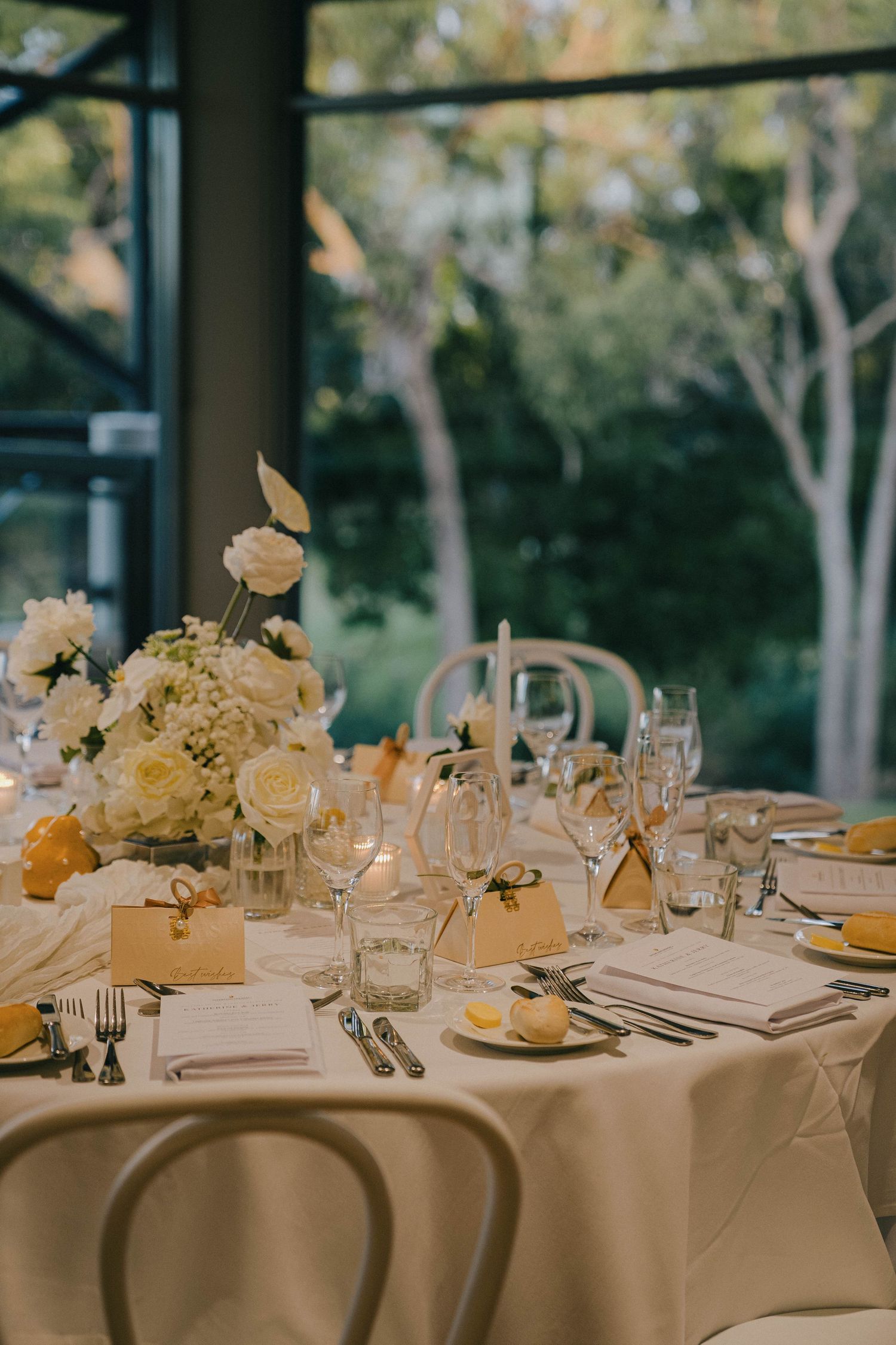 Elegant wedding reception table settings with white roses and candles on cream tablecloths in an outdoor venue.