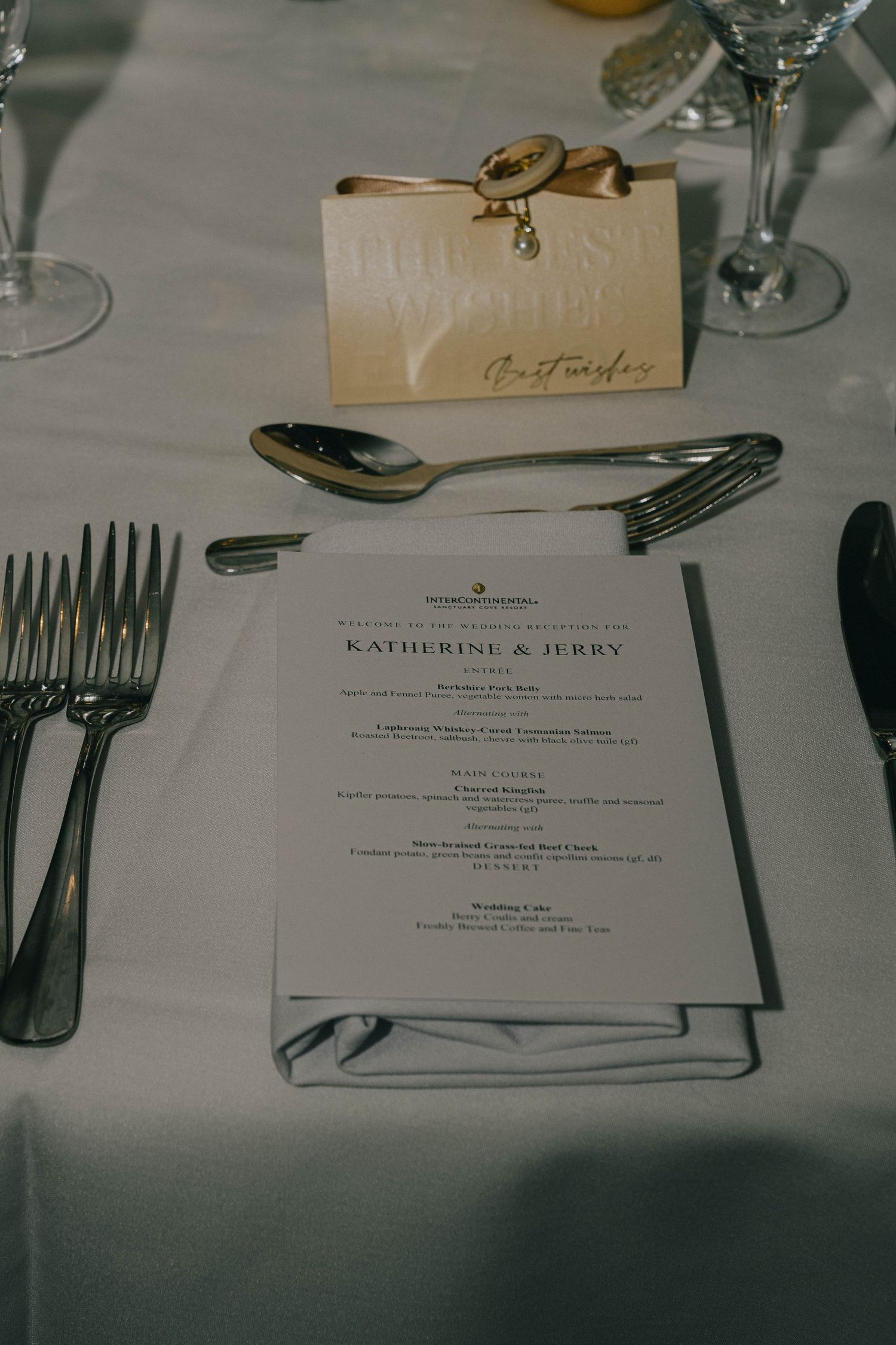 Place settings at a formal dinner with menus and silverware arranged on a white tablecloth.