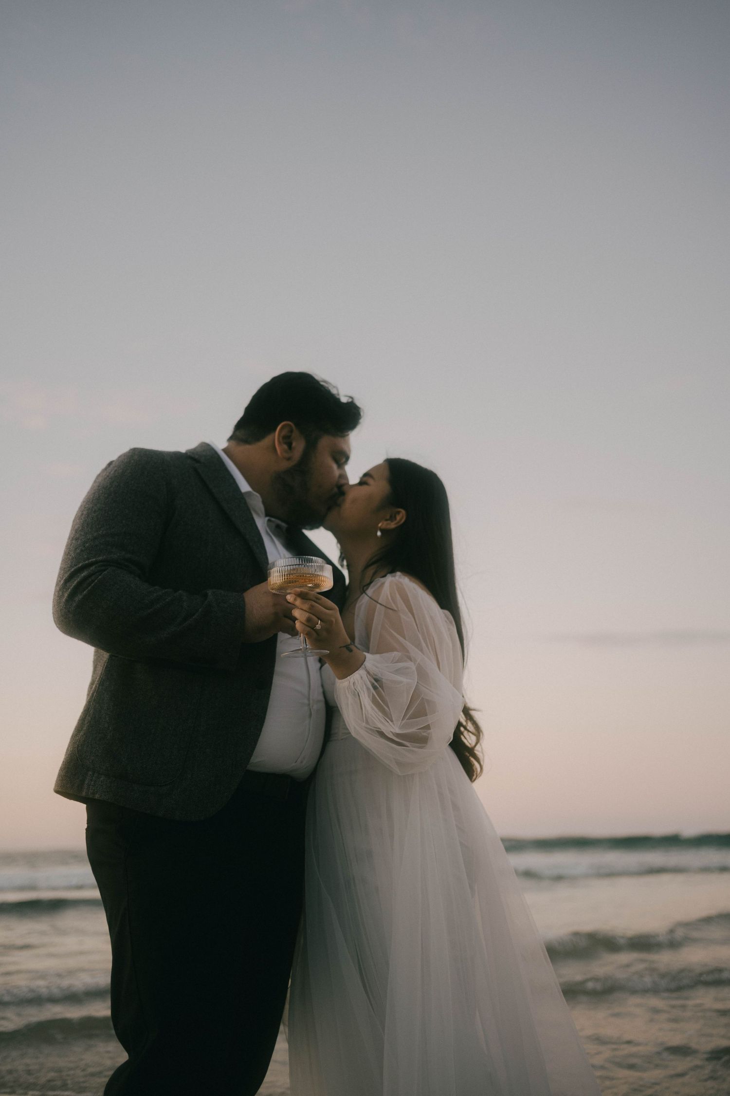 Romantic silhouette of couple sharing intimate moments at sunset on a beach with ocean backdrop.