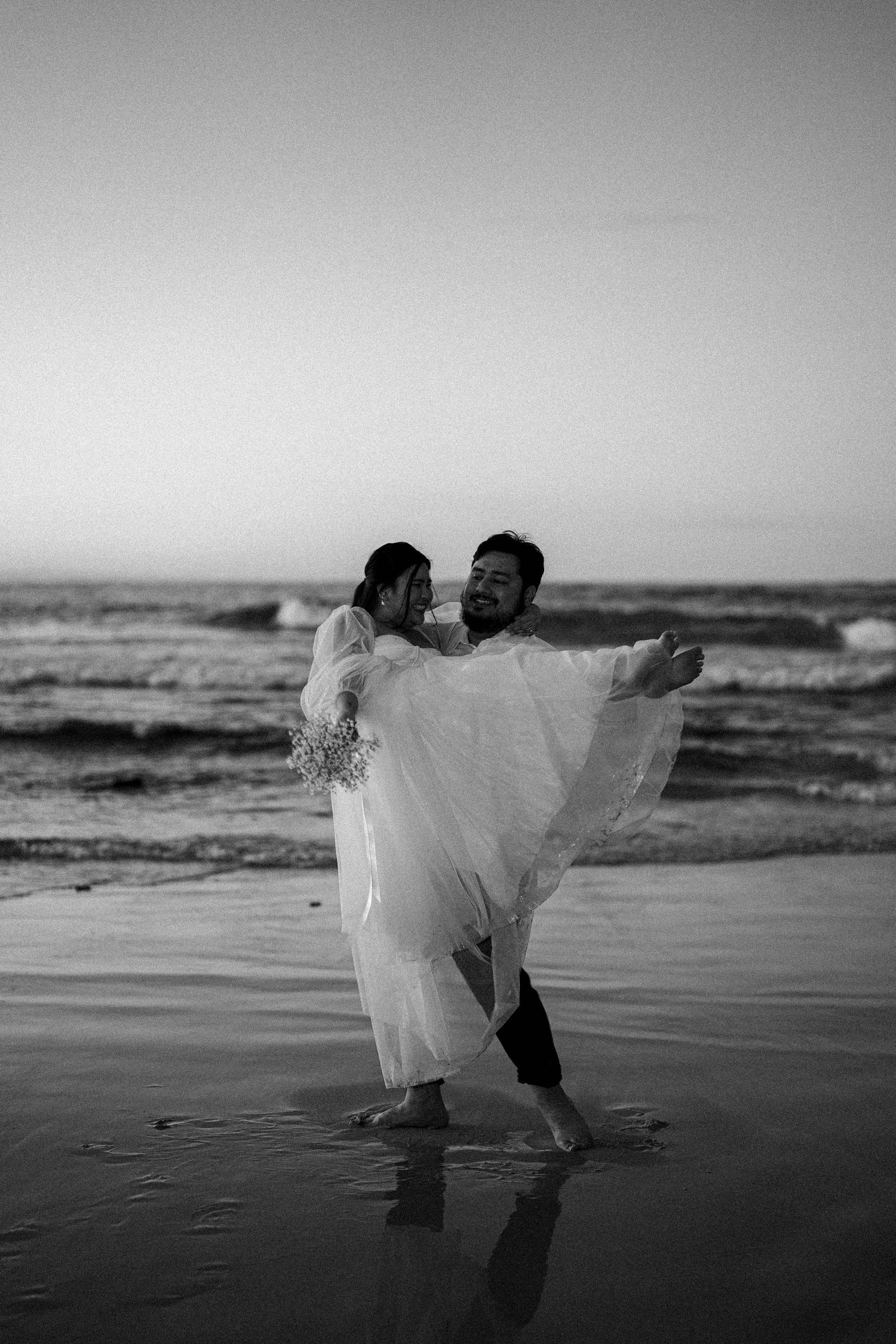 A romantic black and white beach photoshoot sequence shows a couple dancing with the bride's veil flowing in the wind.