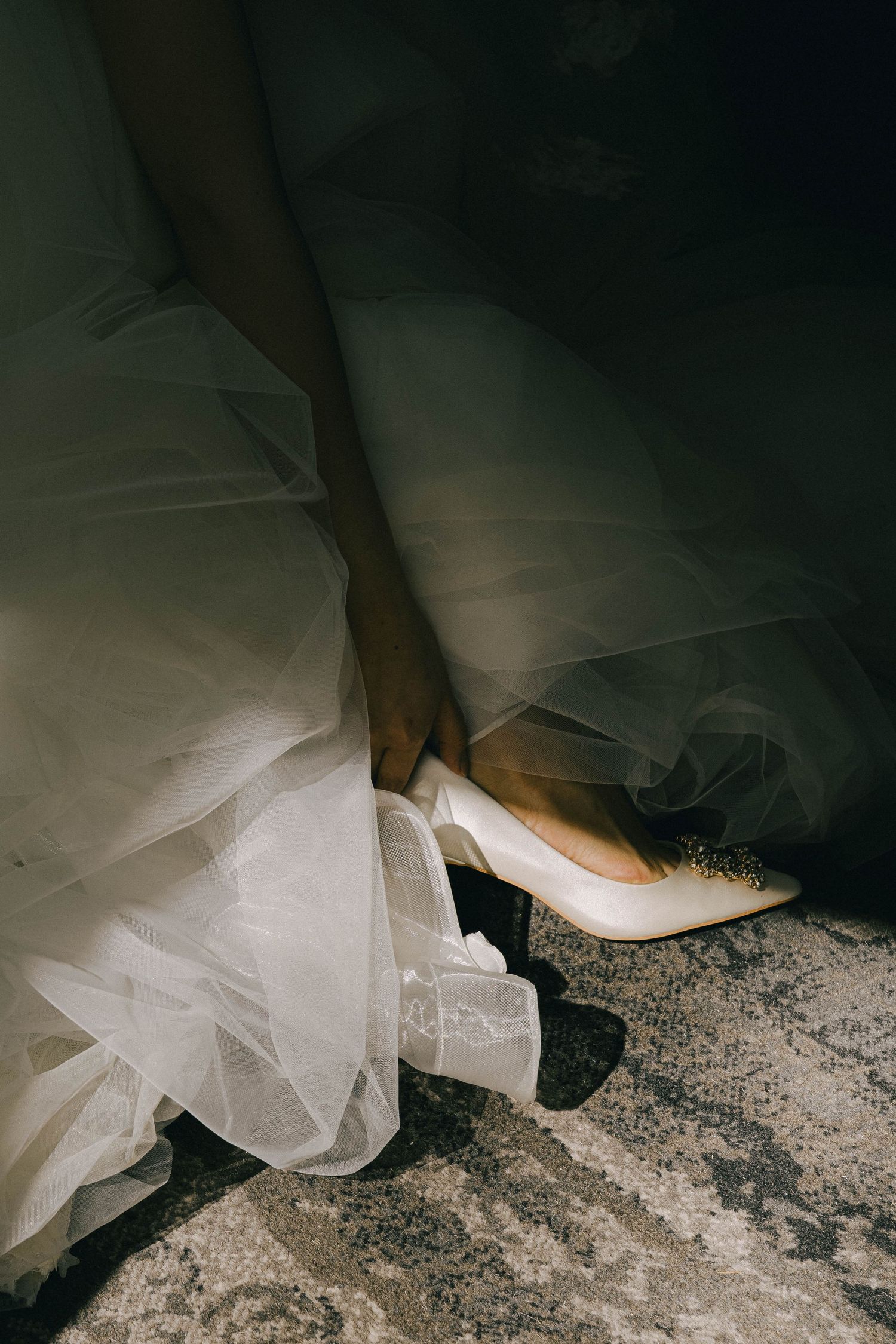 Close-up view of a white wedding dress train and black shoes against a textured stone floor.
