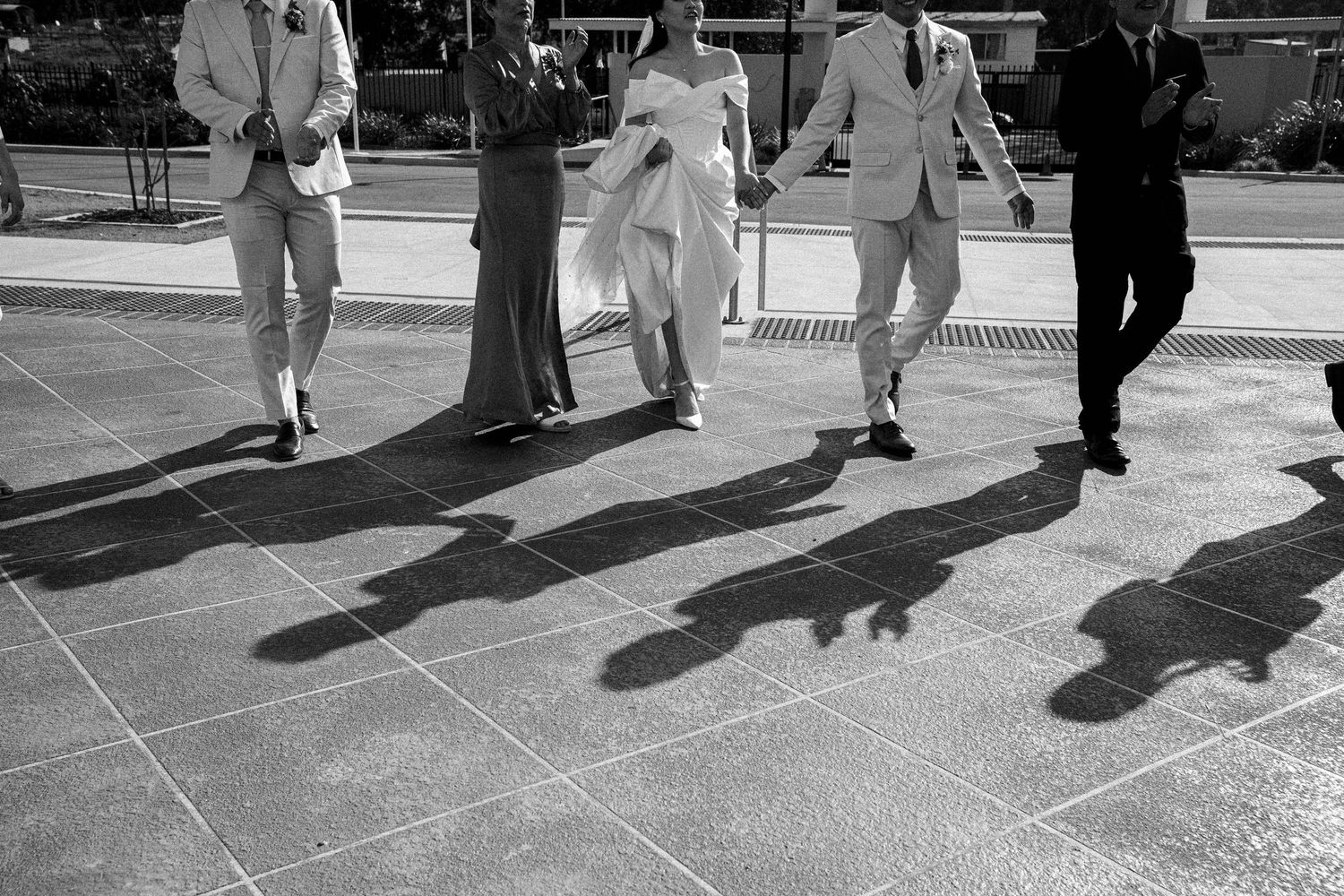 People walking on a sidewalk cast long shadows in black and white photography.