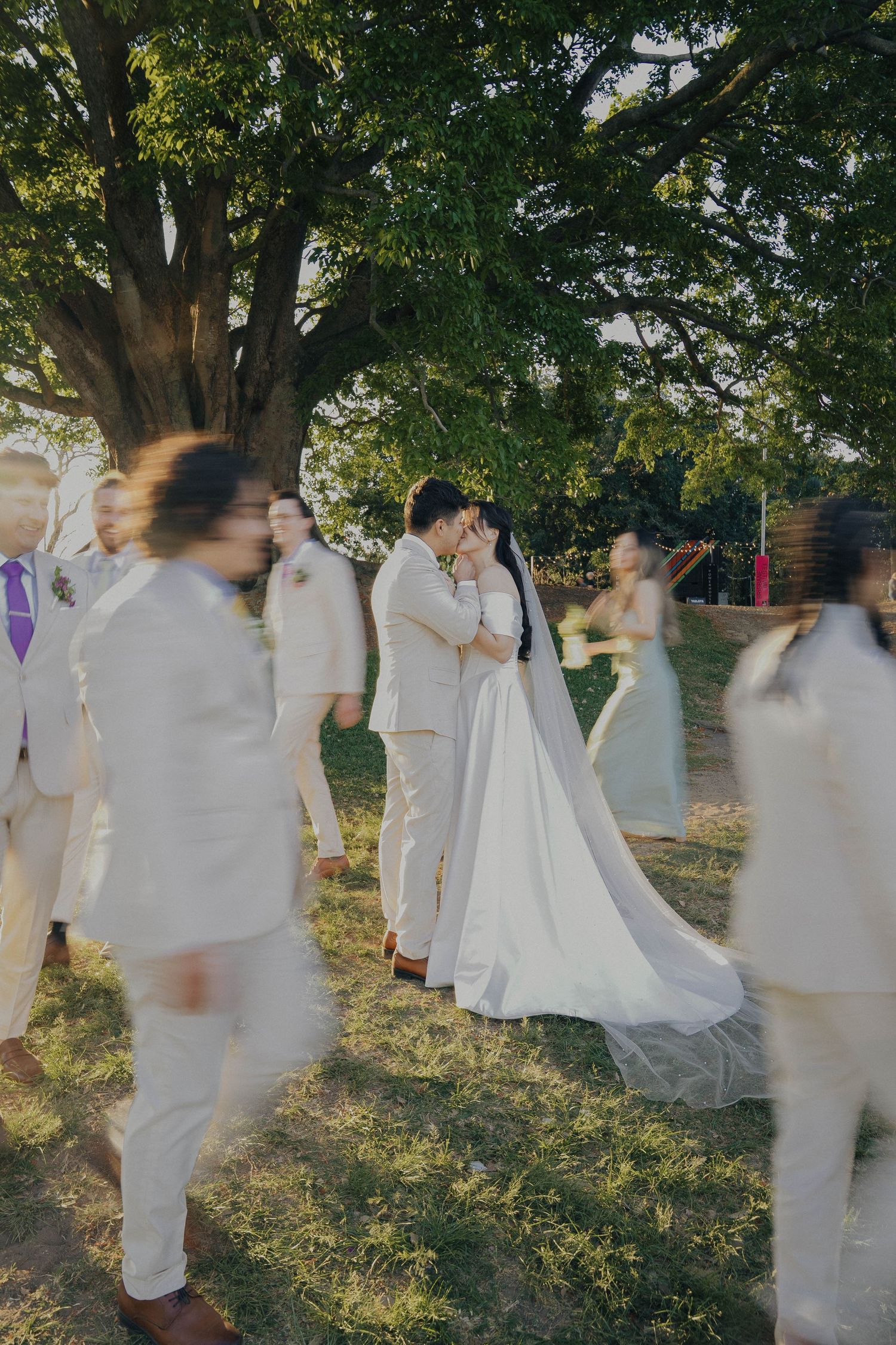 A series of motion-blurred figures in white clothing moving through a sunlit garden setting.