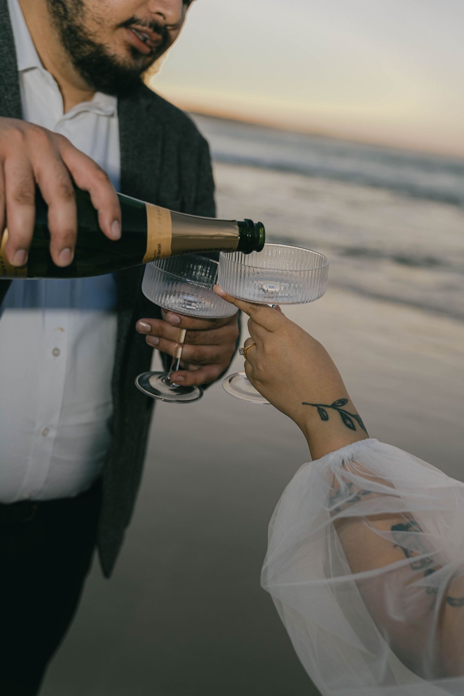 Someone pours champagne into glasses during a sunset celebration at the beach.