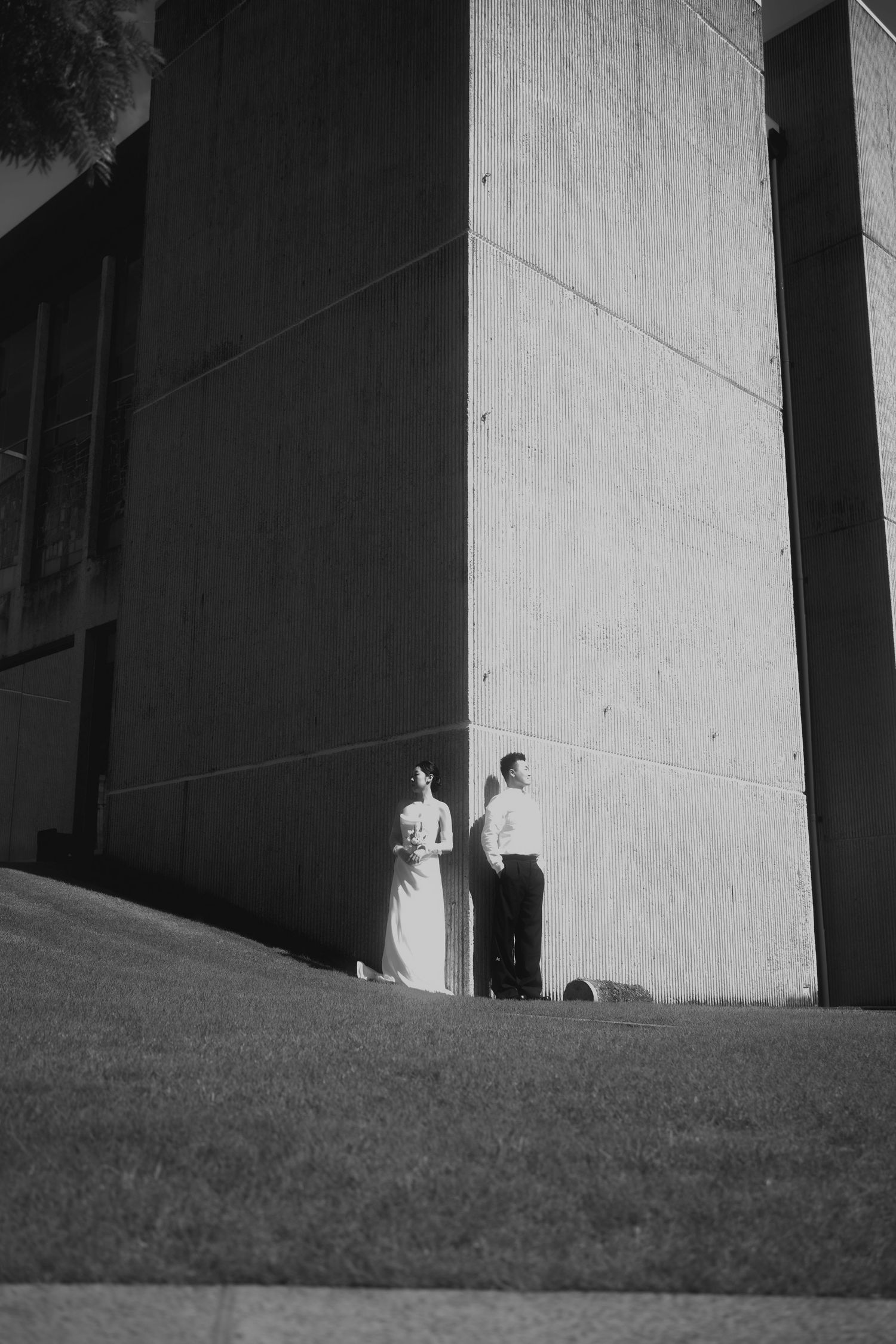 A black and white series of minimalist architectural photos showing figures standing on a grassy slope against stark walls.