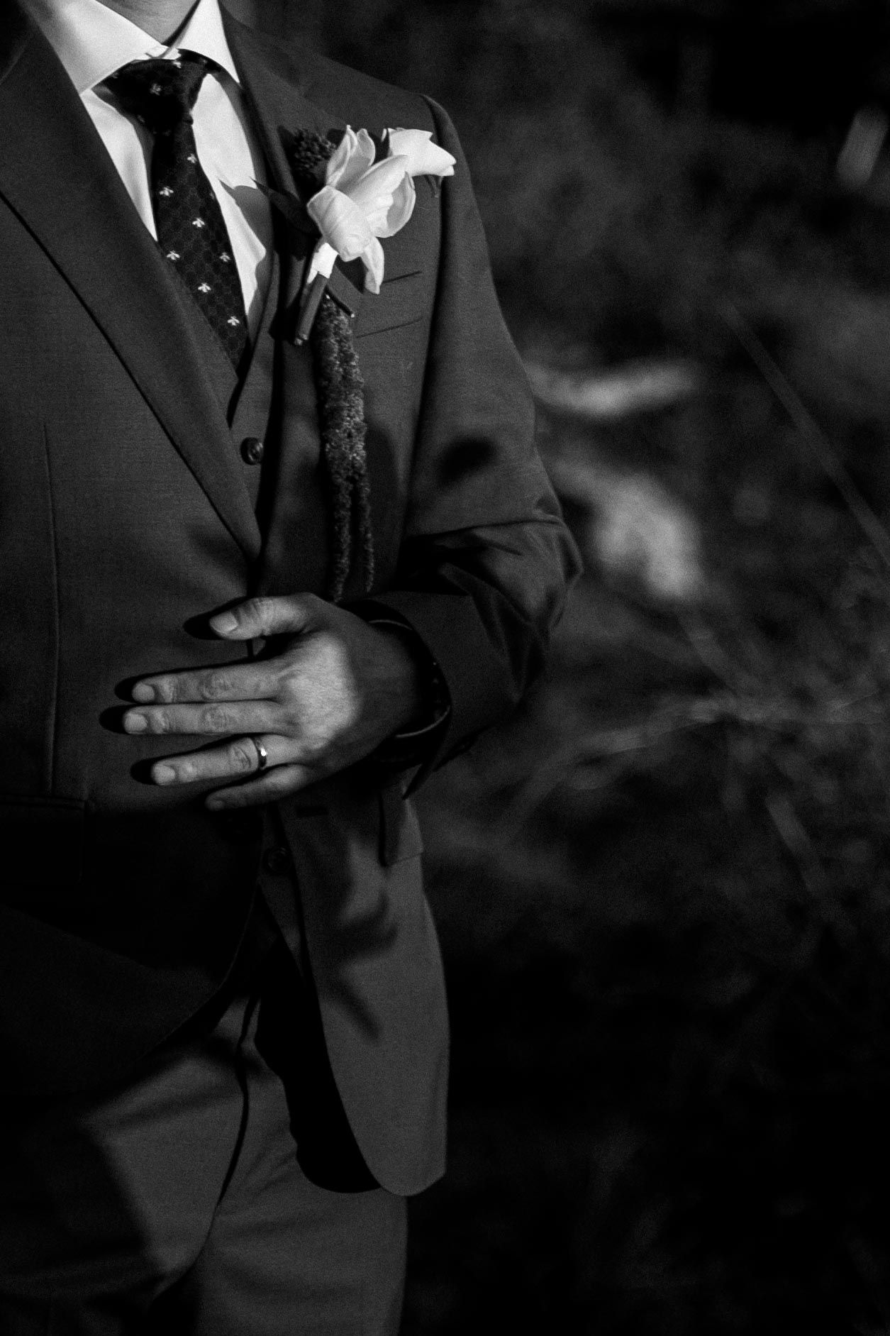 Several black and white detail shots show the torso and hands of someone wearing a formal black suit with white shirt and boutonniere.