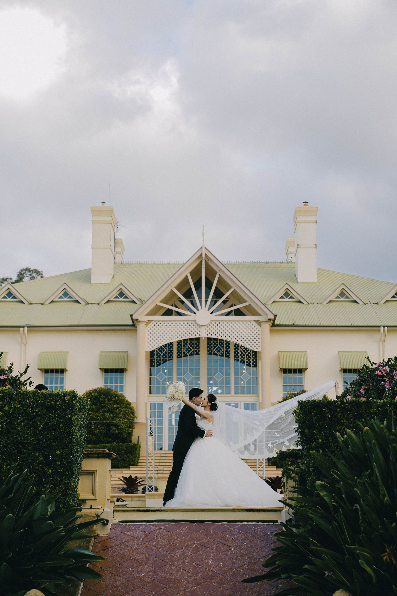 A panoramic sequence showing a wedding couple in front of an elegant white mansion with arched windows and green landscaping.