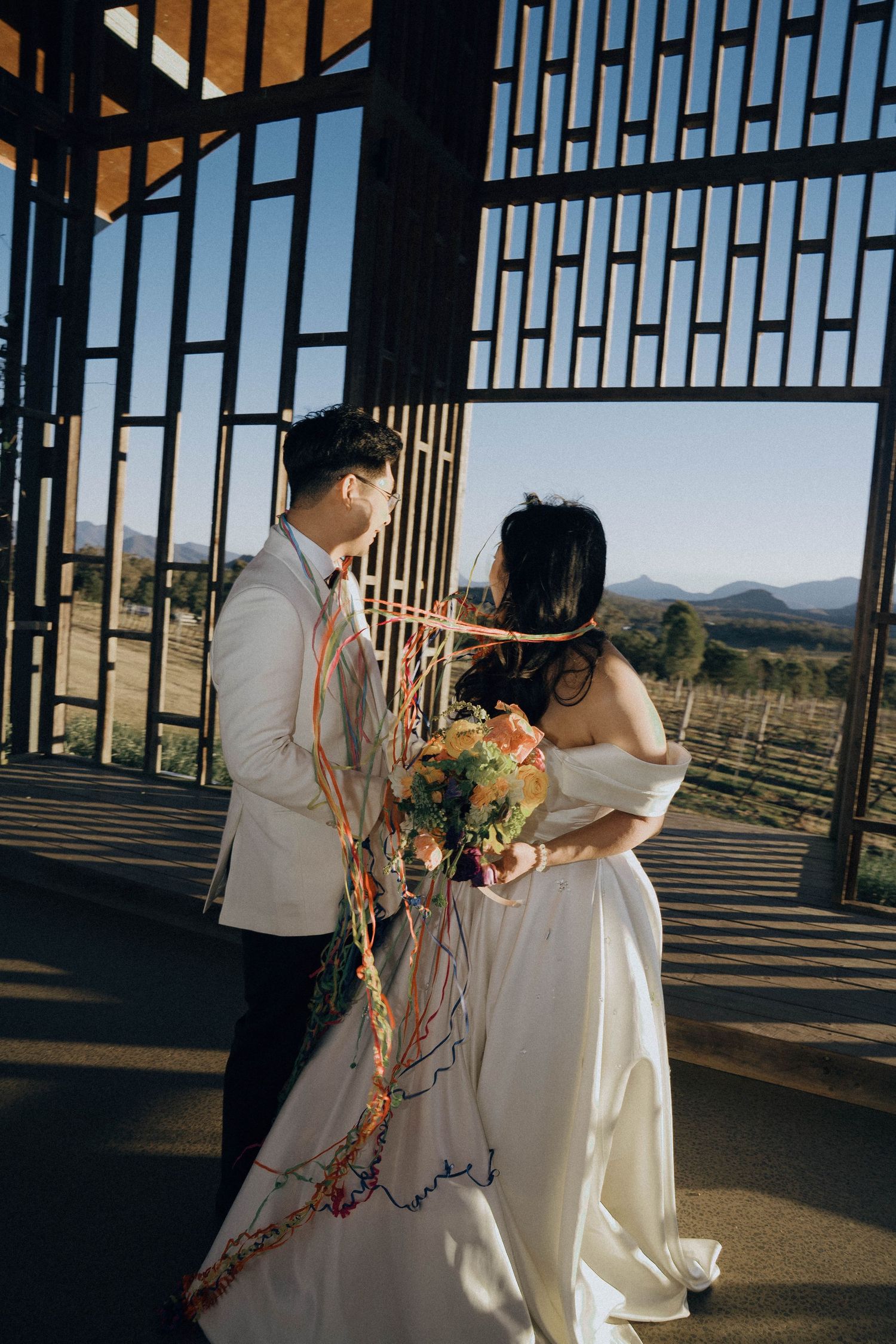 A couple shares an intimate moment at sunset in a rustic wooden pavilion with mountain views in the background.
